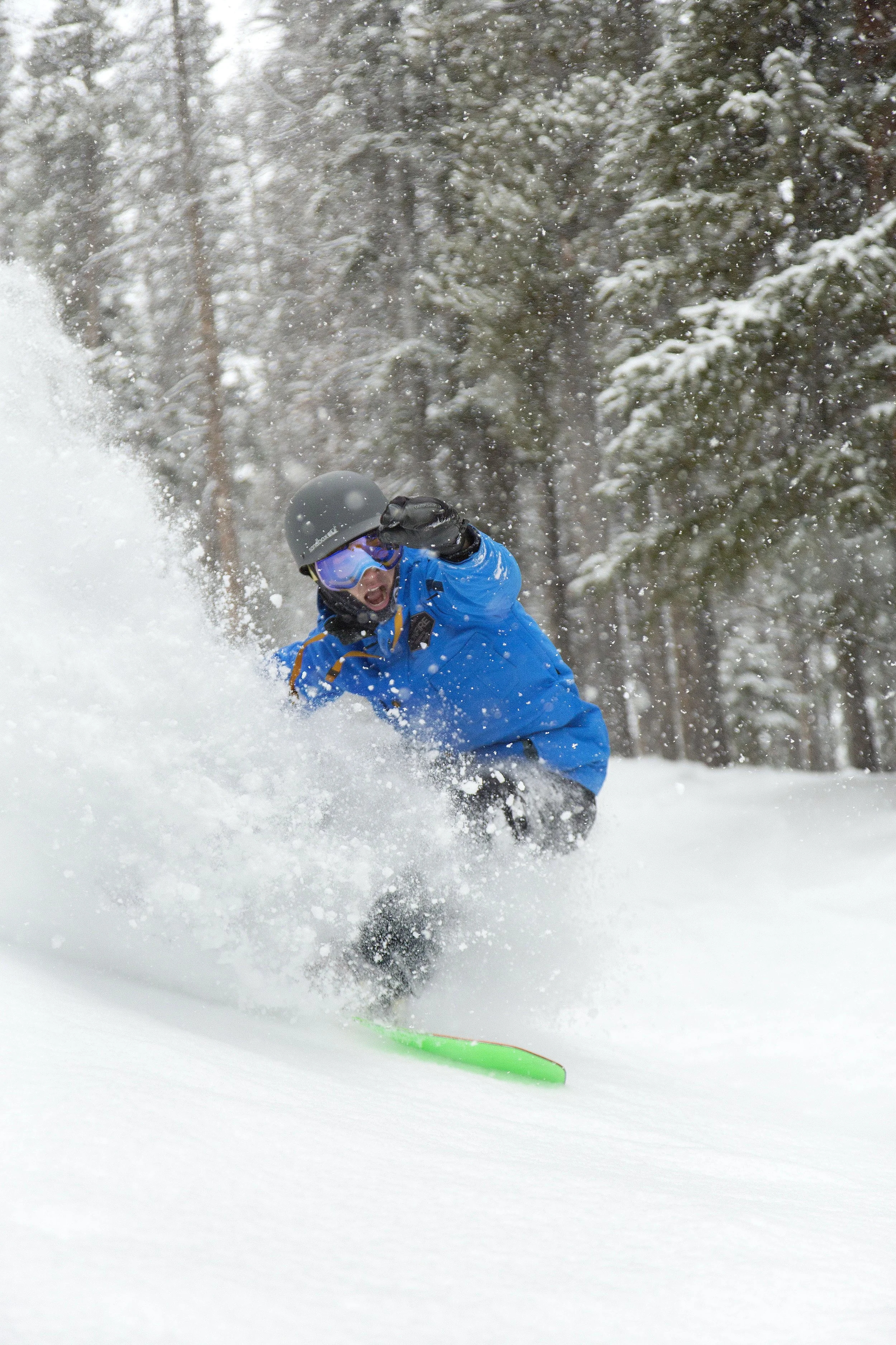 A person skiing down a snowy slope surrounded by snow-covered trees, wearing a blue jacket, helmet, and goggles.