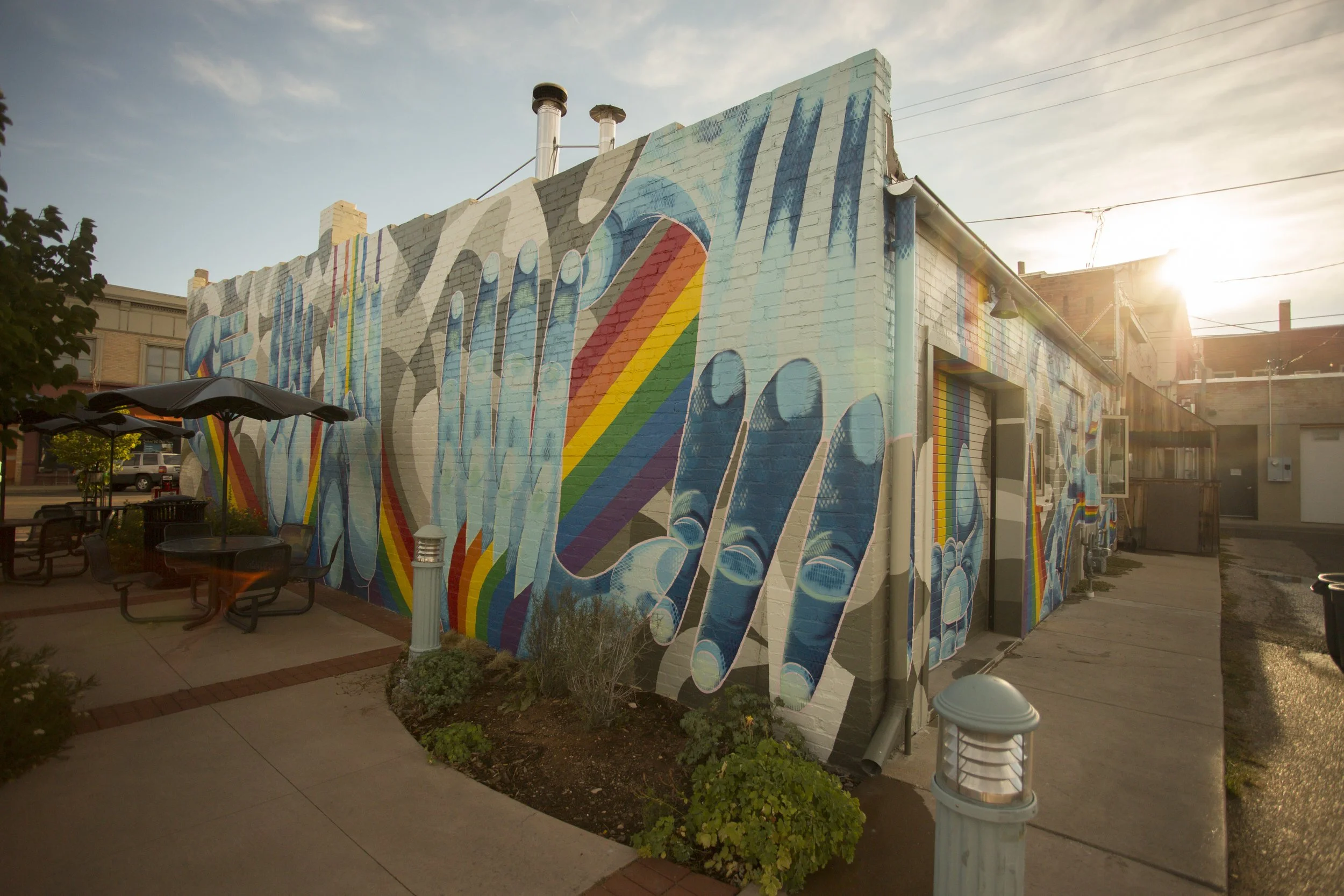Colorful mural of floating hands with painted rainbow on a brick building at sunset.