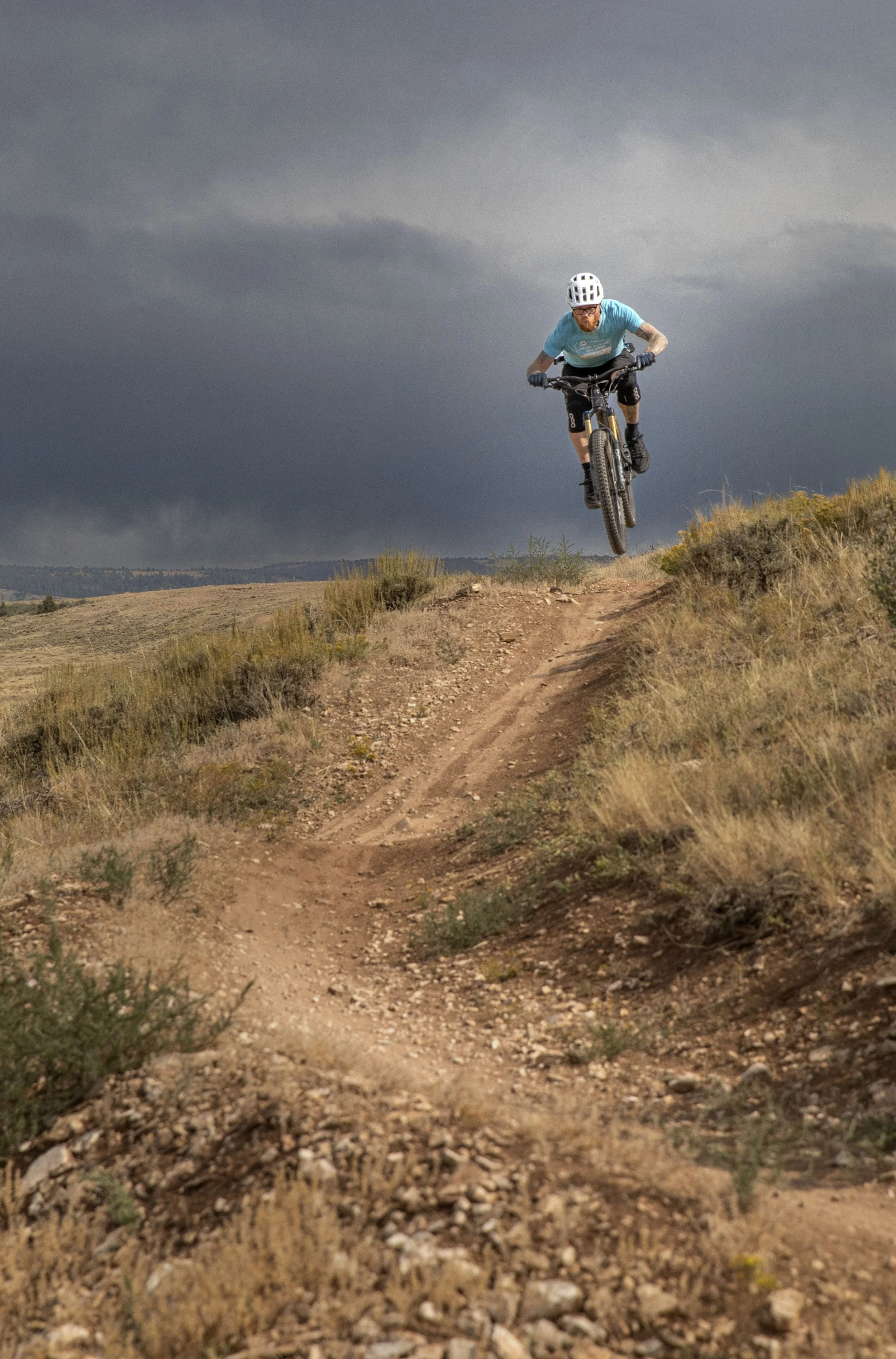 A person mountain biking on a trail with dark storm clouds in the sky.