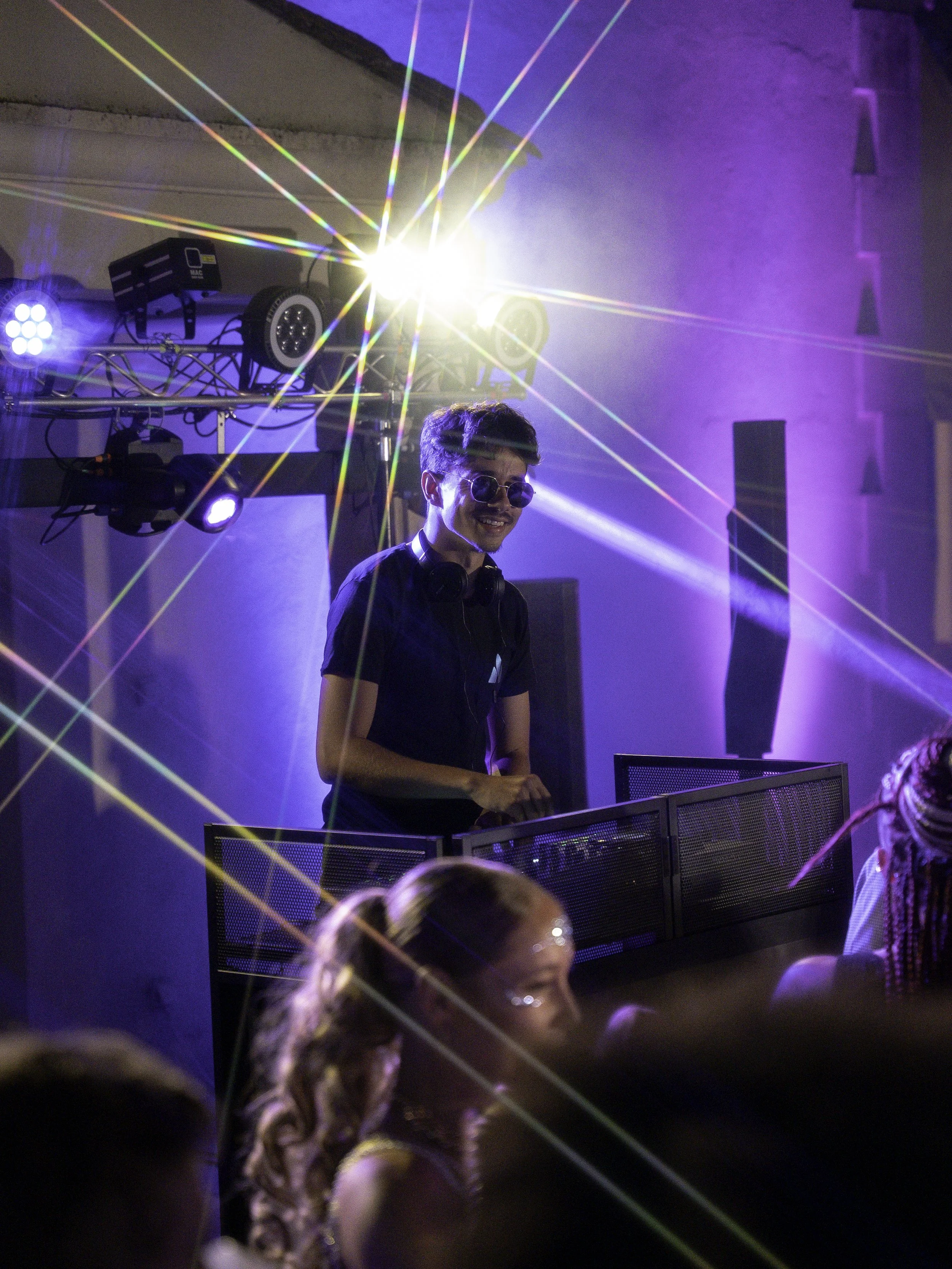 Jeune DJ portant des lunettes de soleil, souriant, jouant de la musique lors d'une fête avec éclairage coloré et laser.