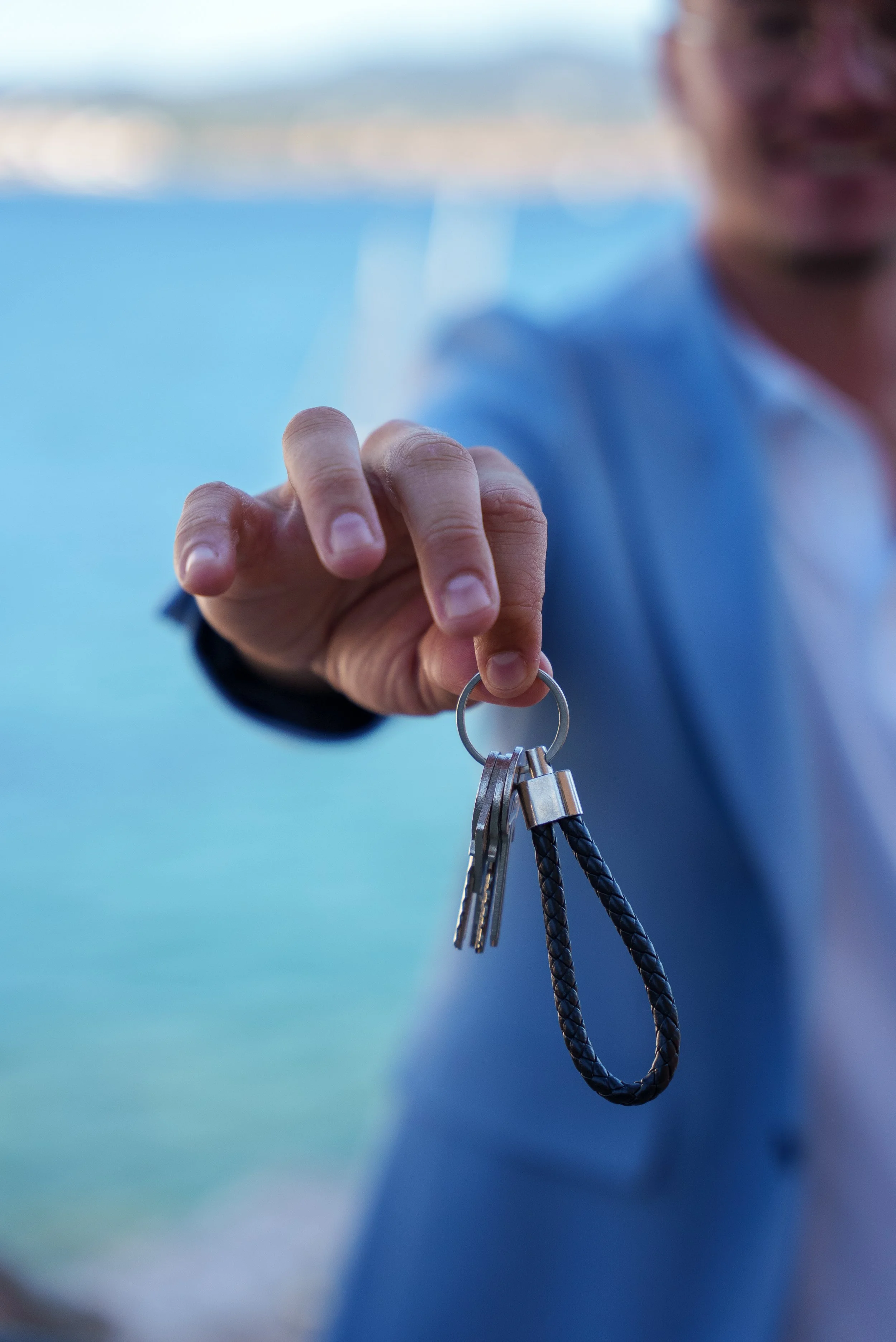 Une personne tenant un porte-clés avec plusieurs clés, en extérieur avec un arrière-plan d'eau et de paysage flou.