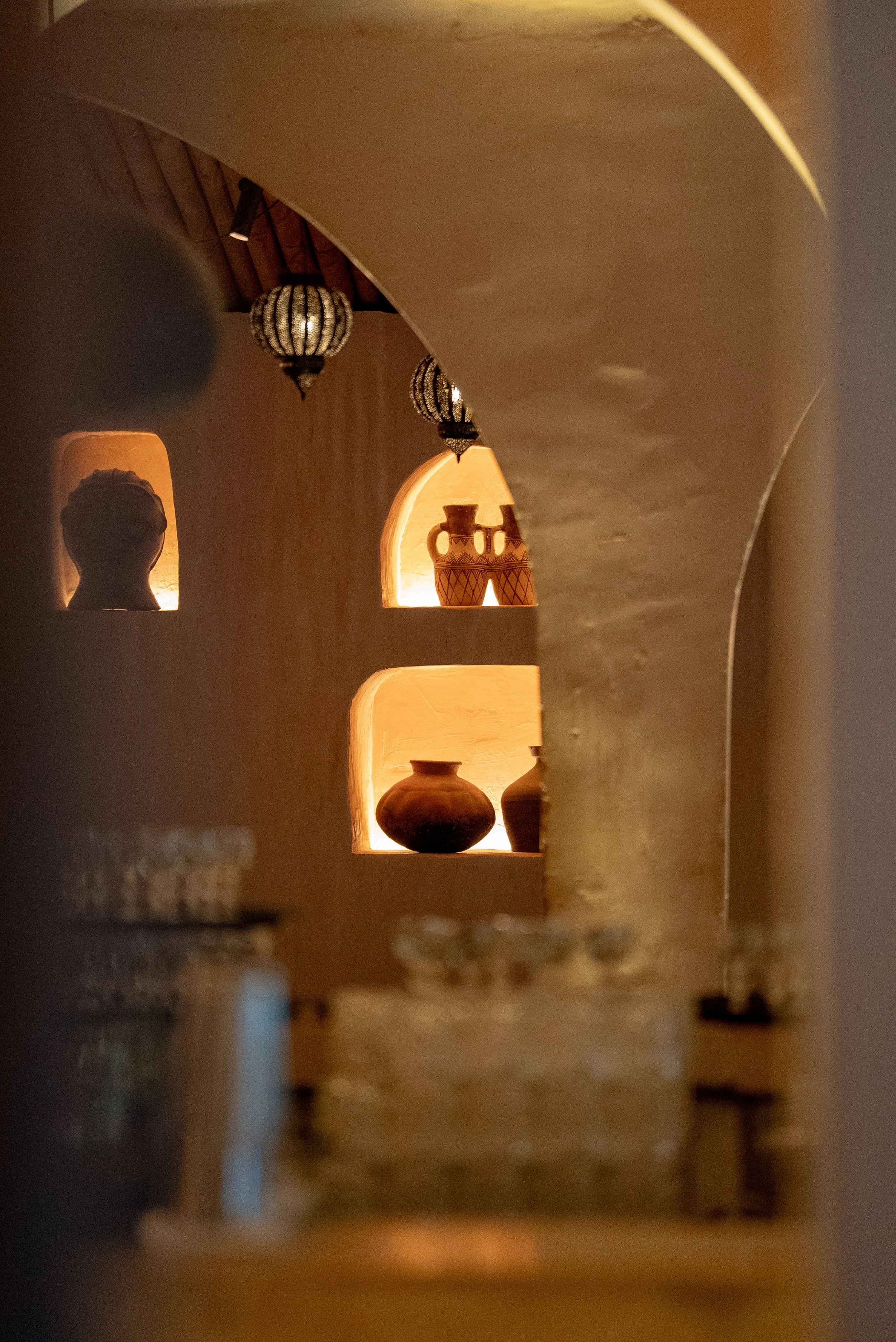 Vase en céramique dans une niche, décorée avec des lampes suspendues en forme de globe, dans un mur en plâtre beige, ambiance chaleureuse et tamisée.