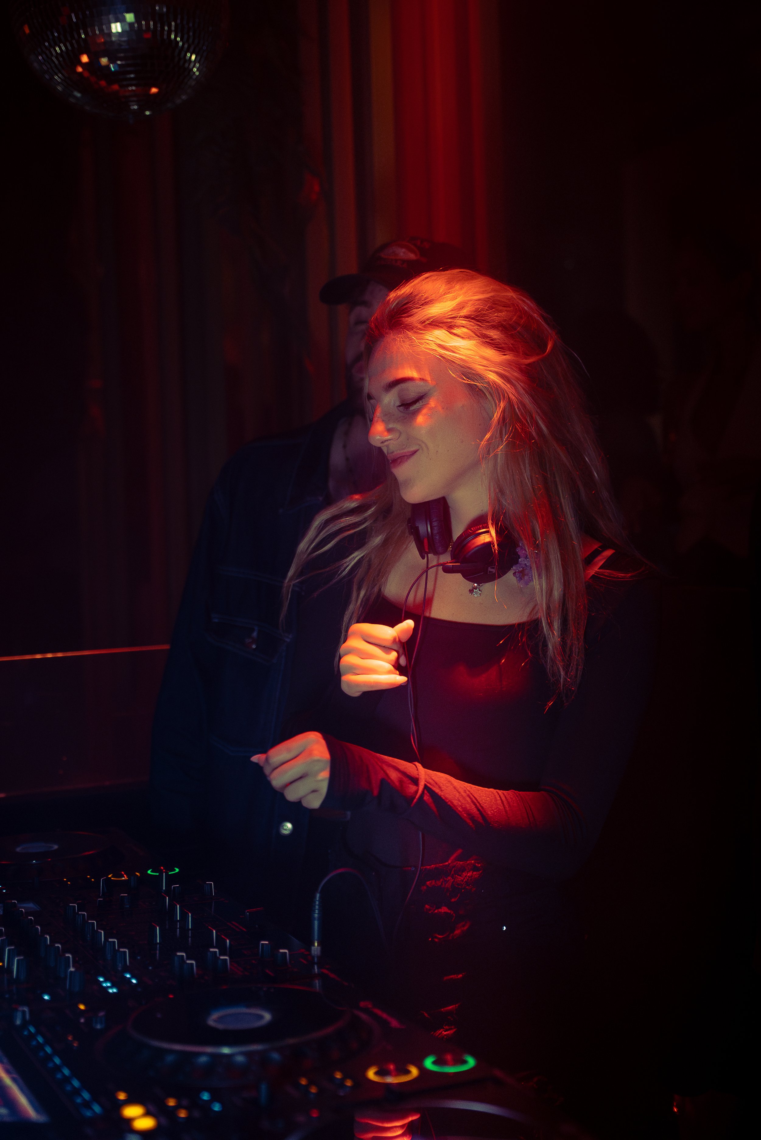 Jeune femme DJ avec des écouteurs, dans une ambiance de nuit avec des lumières rouges, utilisant un équipement de DJ, dans un club ou à une fête