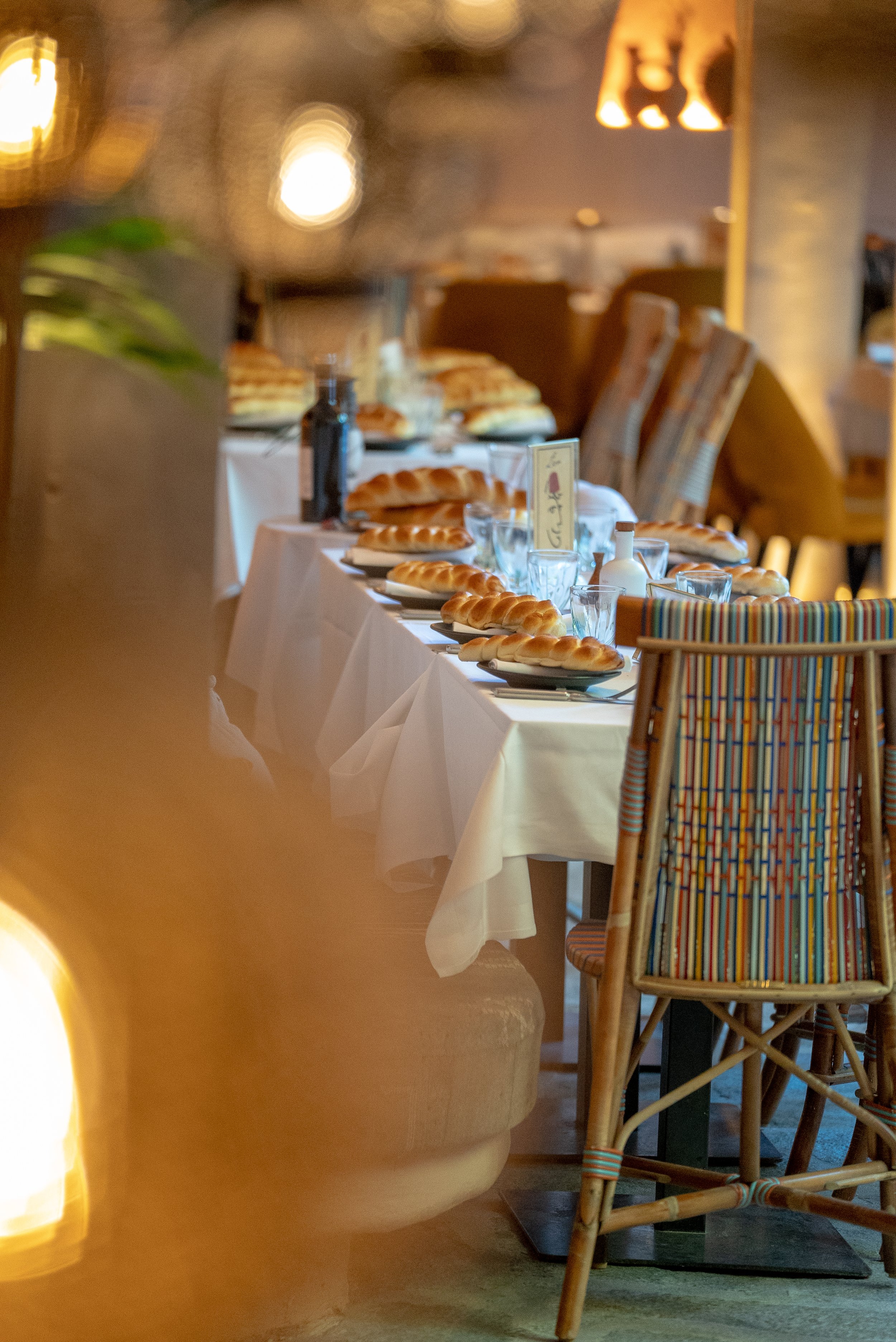 Une table de restaurant élégamment dressée avec des pains chauds, des verres, des bouteilles, et une décoration chaleureuse dans un style rustique, prête pour un repas.