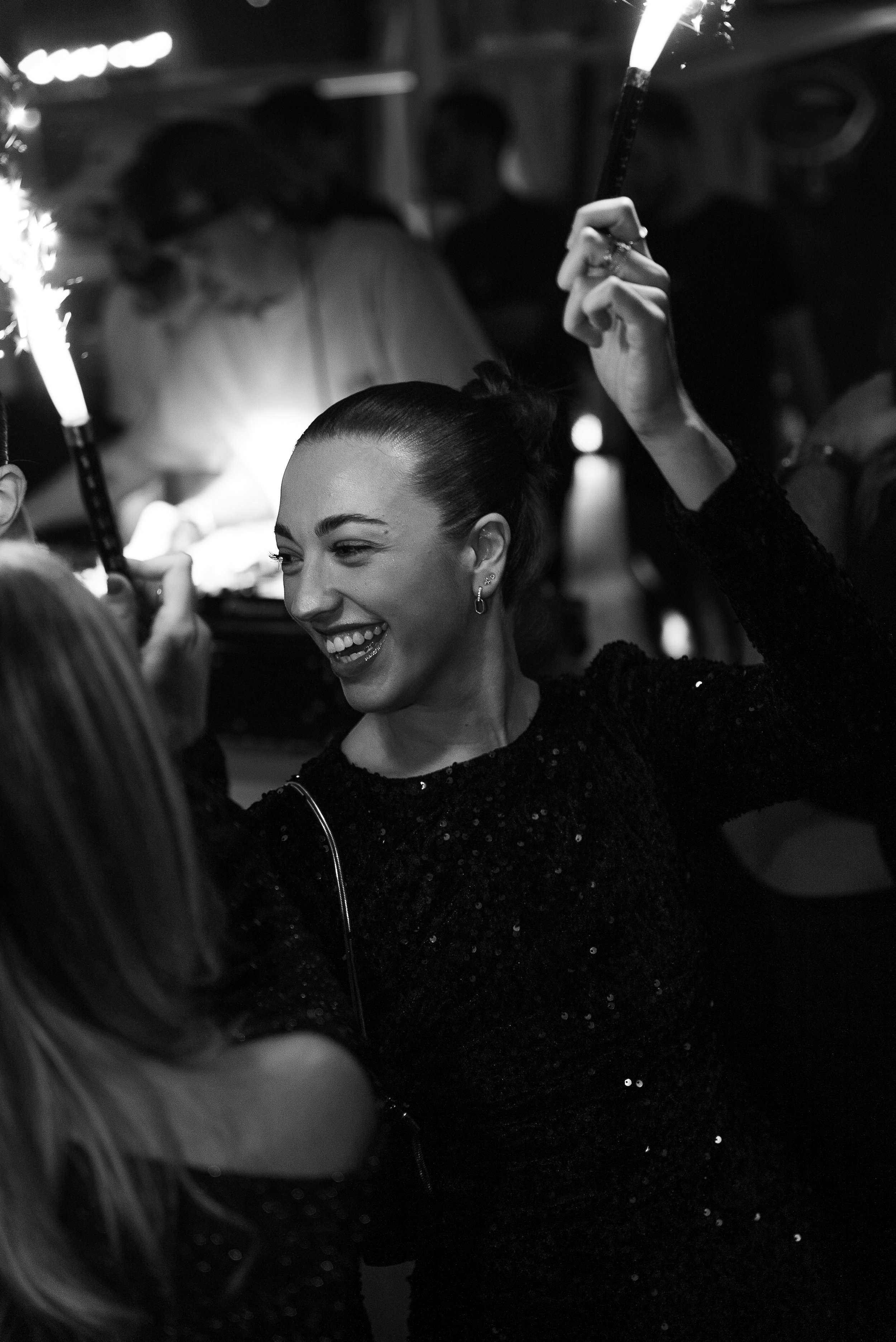 Une femme souriante lors d'une fête ou célébration, tenant une lampe à étincelles, en noir et blanc.
