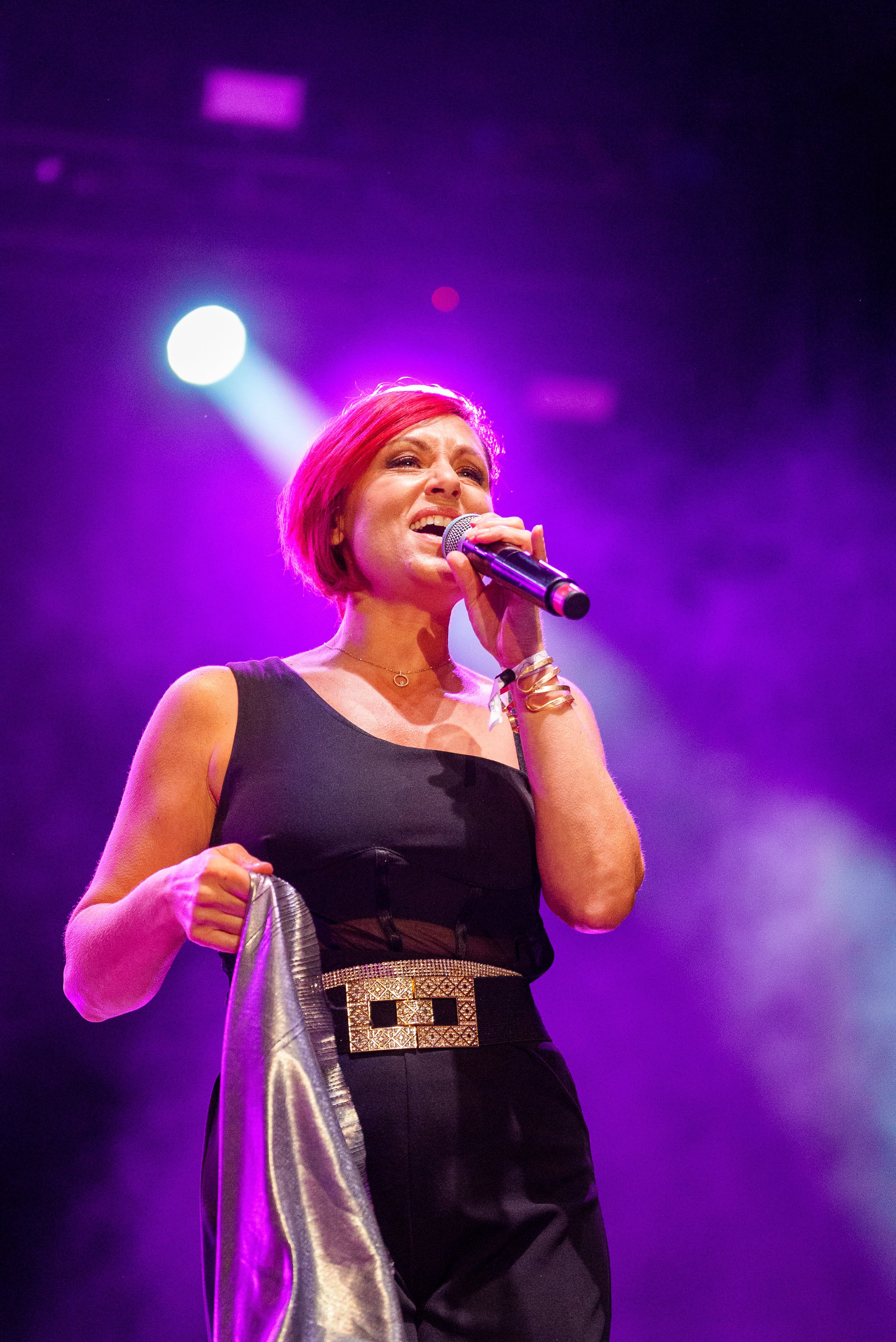 Une femme chante lors d'un spectacle avec des lumières violettes et bleues en arrière-plan.
