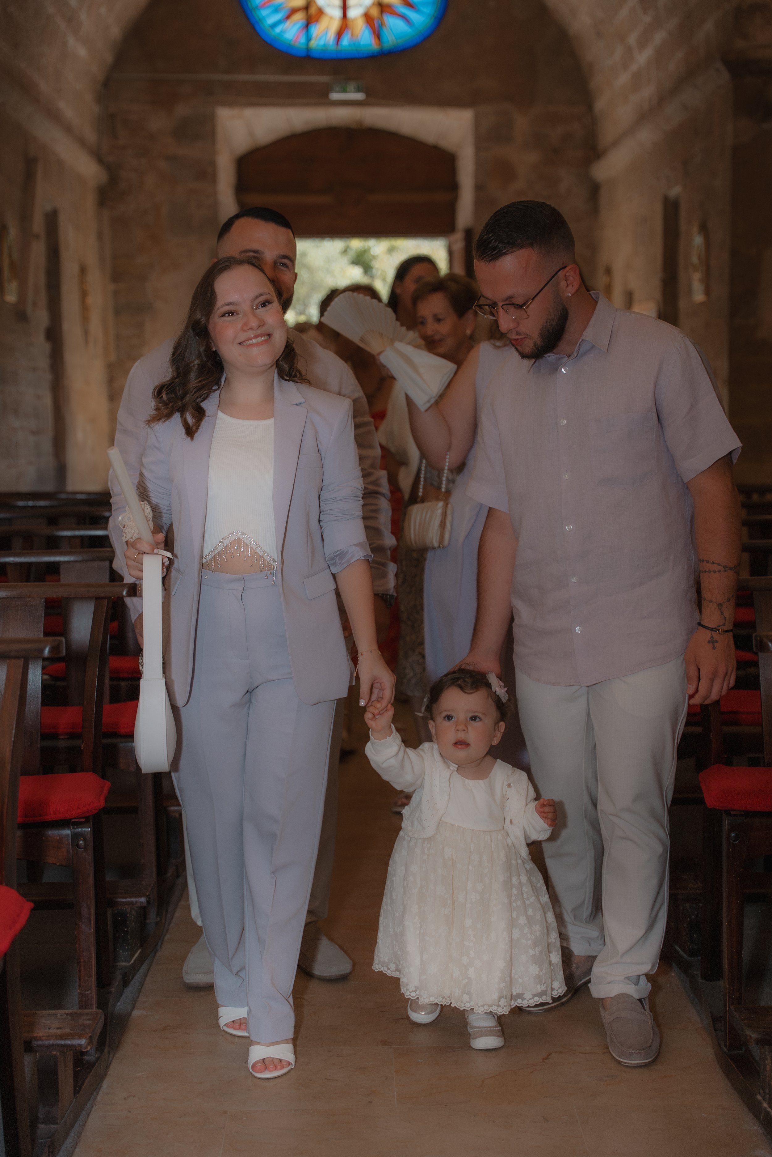 Une famille marche dans une église en célébration. La petite fille porte une robe blanche et est accompagnée par ses parents.