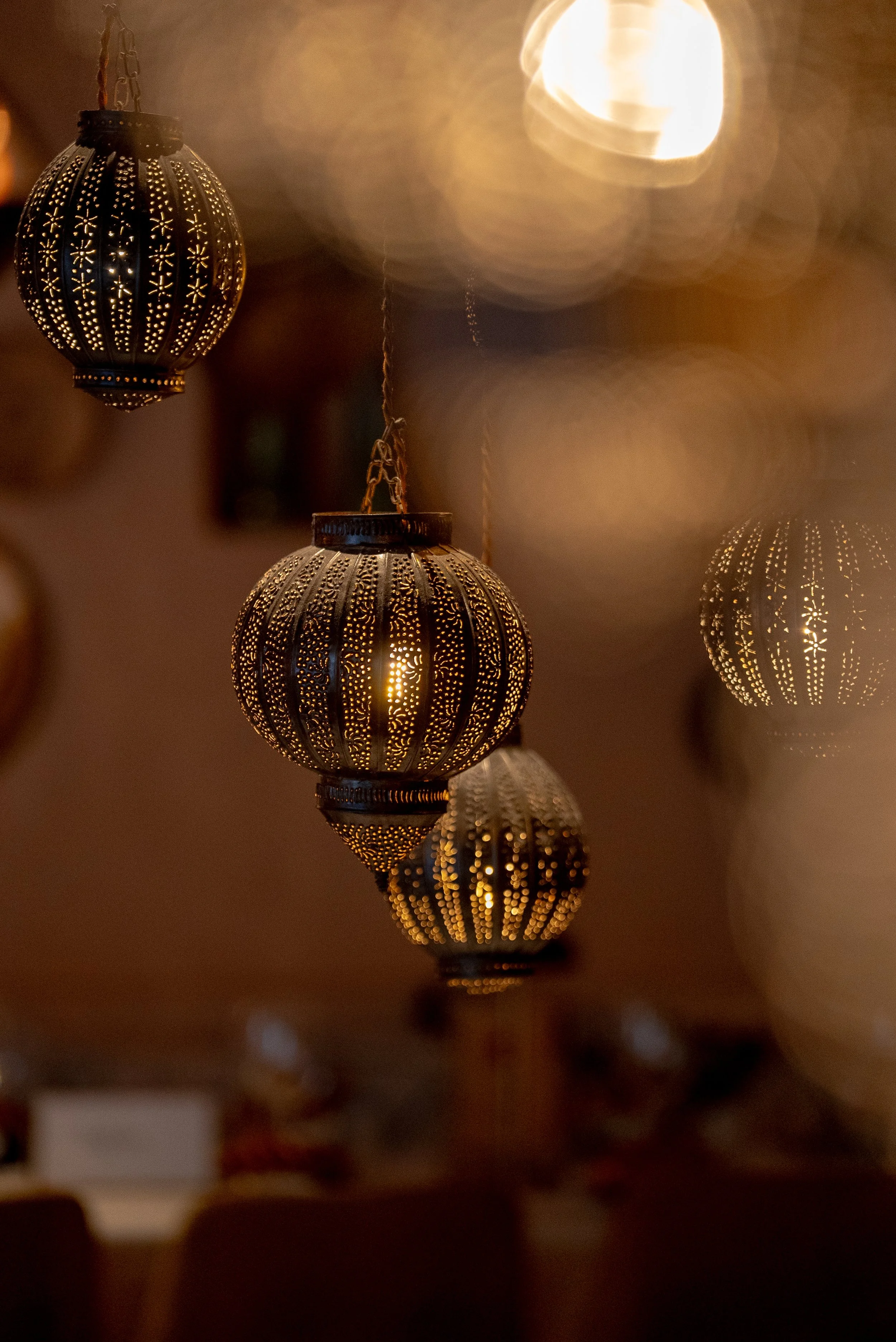 Lampes suspendues en métal avec des perforations, éclairant doucement une pièce dans une ambiance chaleureuse.