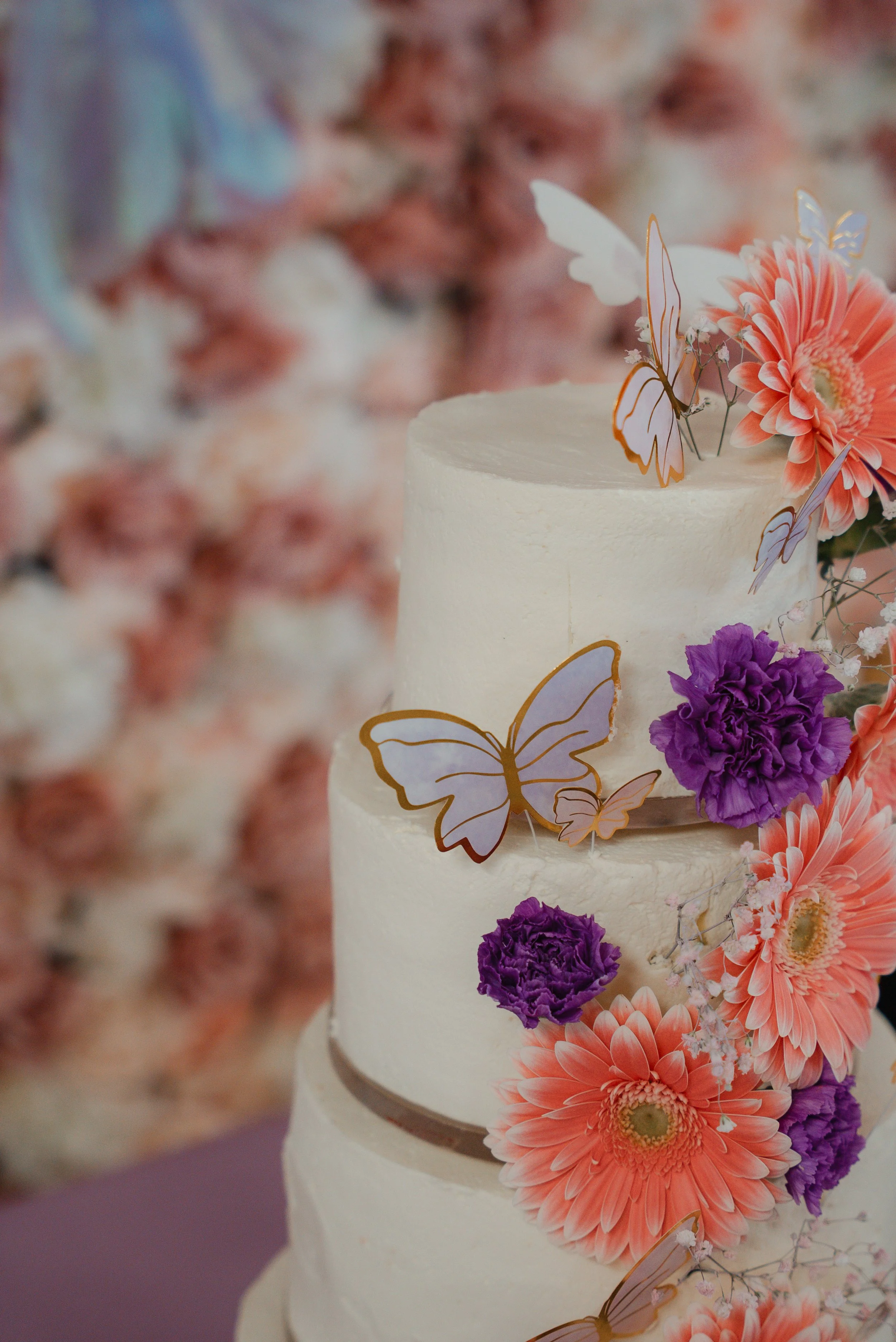 Gâteau de mariage blanc décoré avec des fleurs roses et violettes et des papillons en papier.