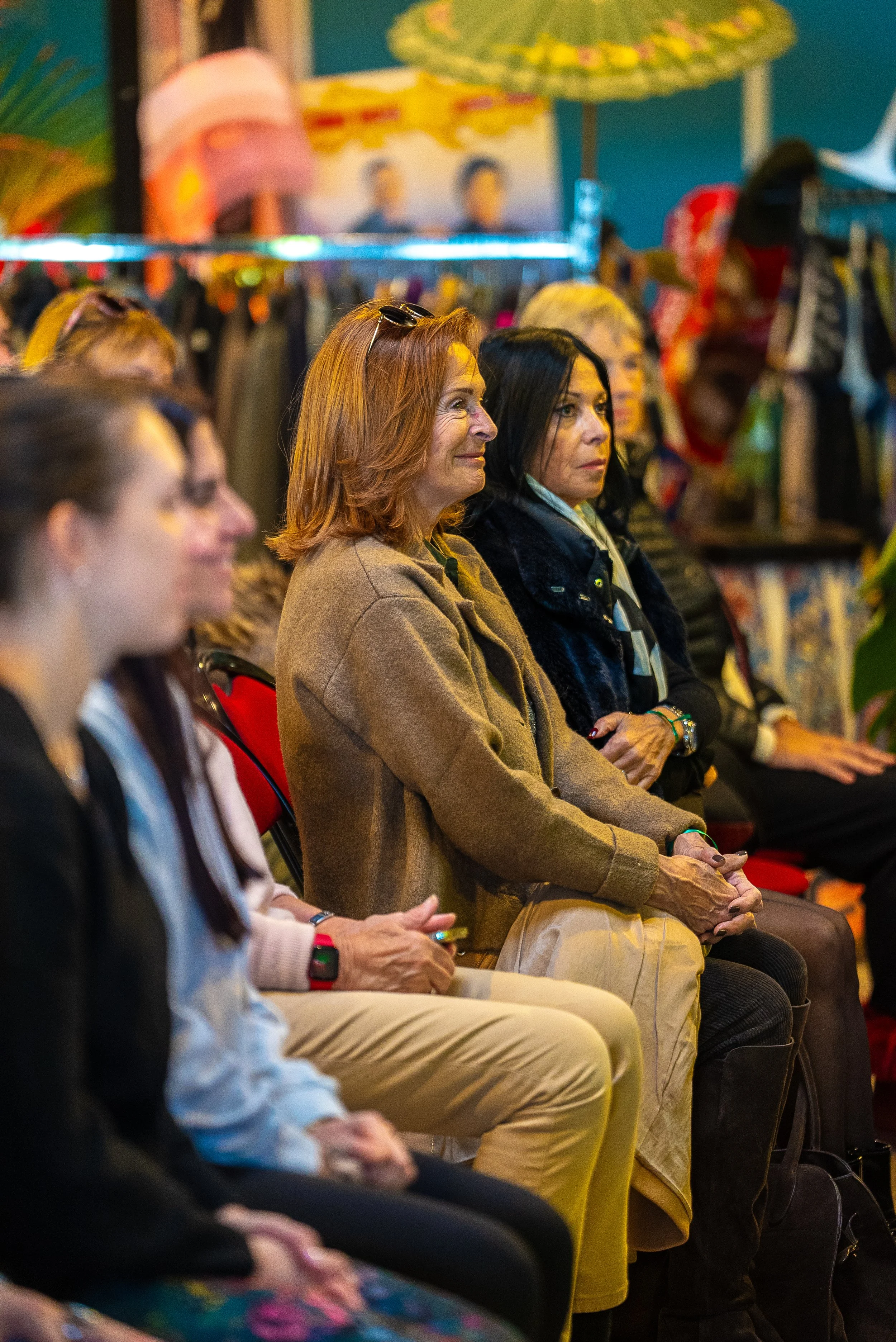 Groupe de femmes assises en ligne à une présentation ou conférence, décor coloré avec des parasols et des œuvres d'art