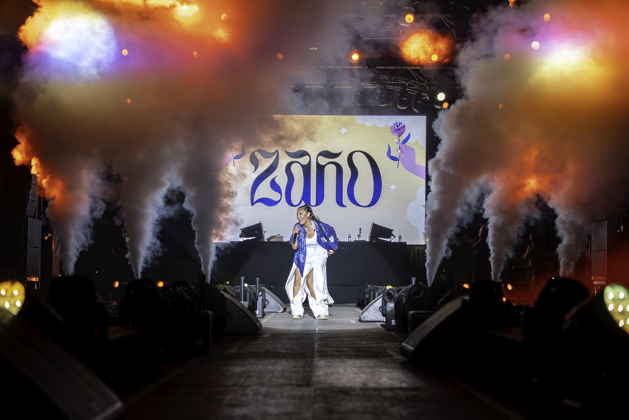 Une chanteuse sur scène lors d'un concert, avec des effets de vapeur et un grand écran derrière affichant '2020'