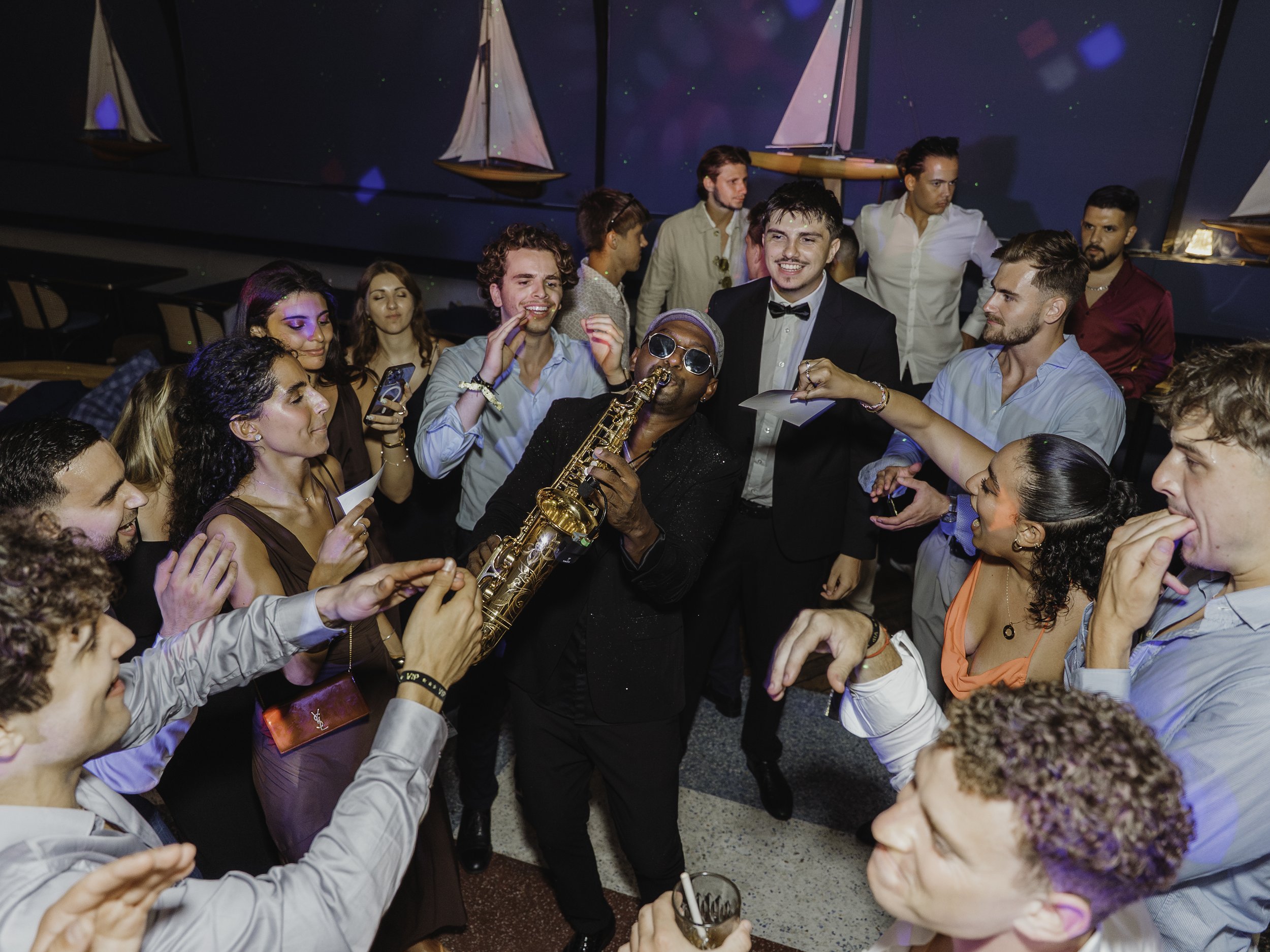 Un groupe de personnes dansant et s'amusant lors d'une fête, avec un musicien jouant du saxophone, dans une ambiance festive.