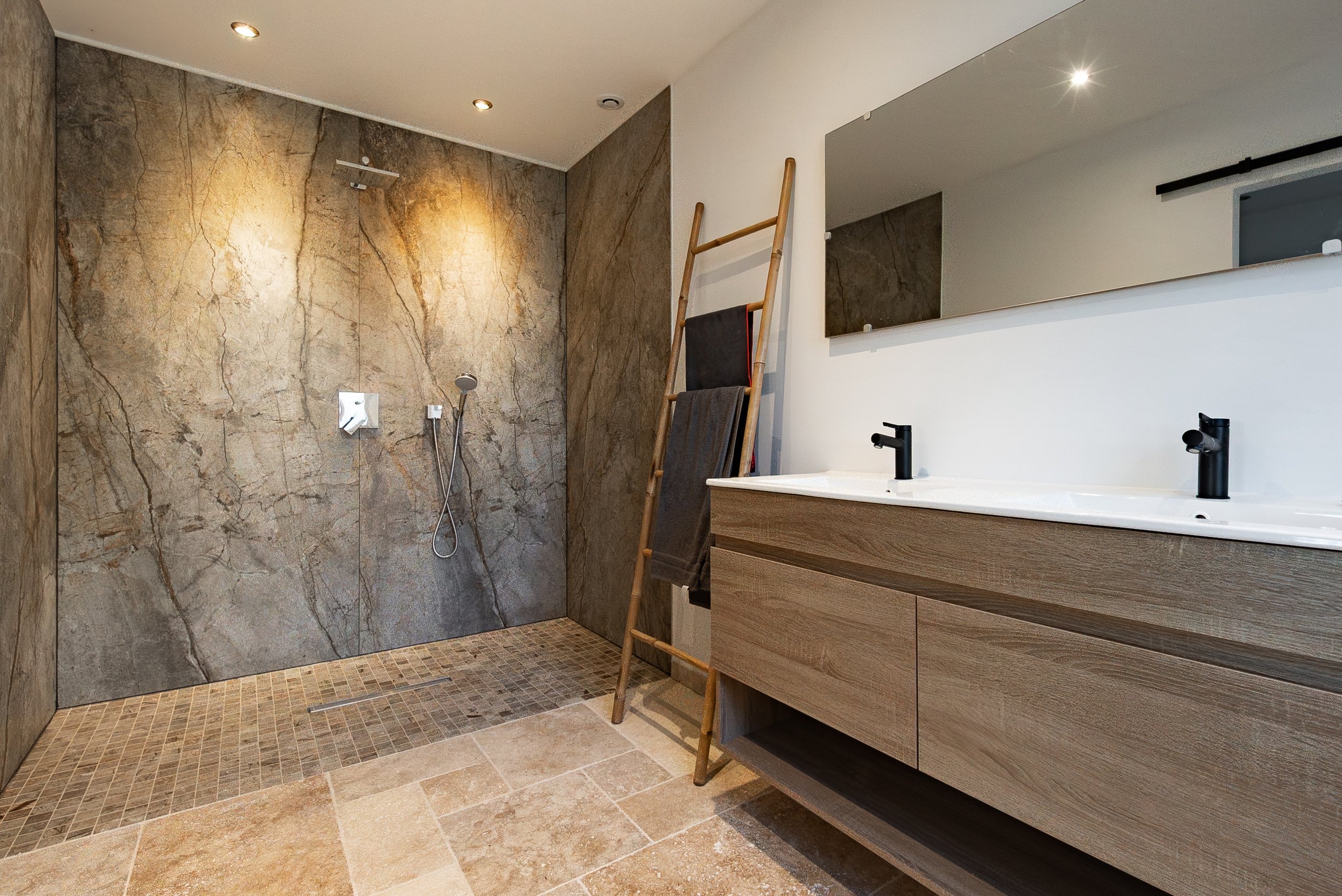 Salle de bain moderne avec douche à l'italienne en pierre, double vasque en bois et grand miroir.