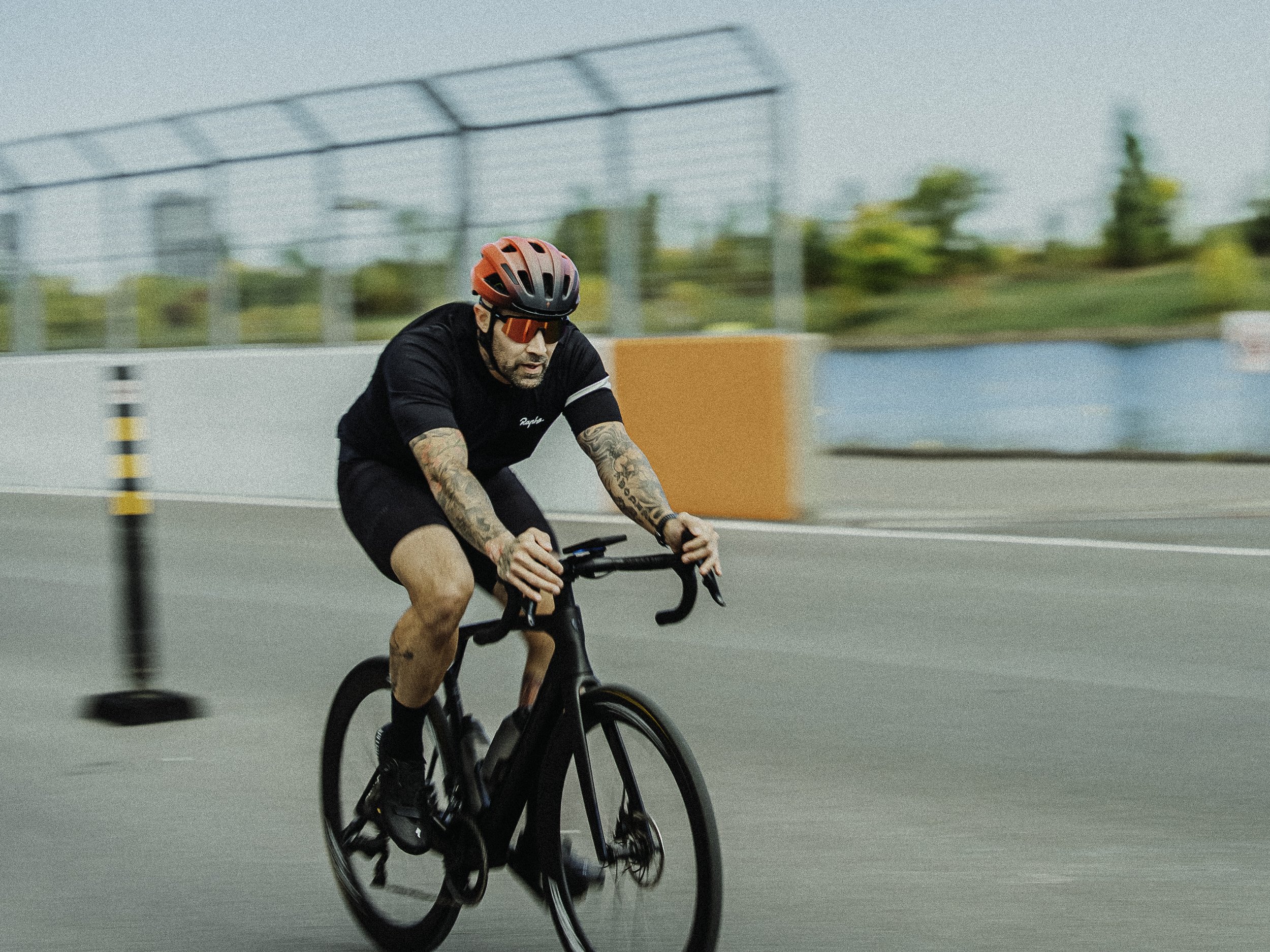 Un homme portant un casque rouge et des lunettes de soleil roule à vélo sur une route avec des barrières de sécurité.