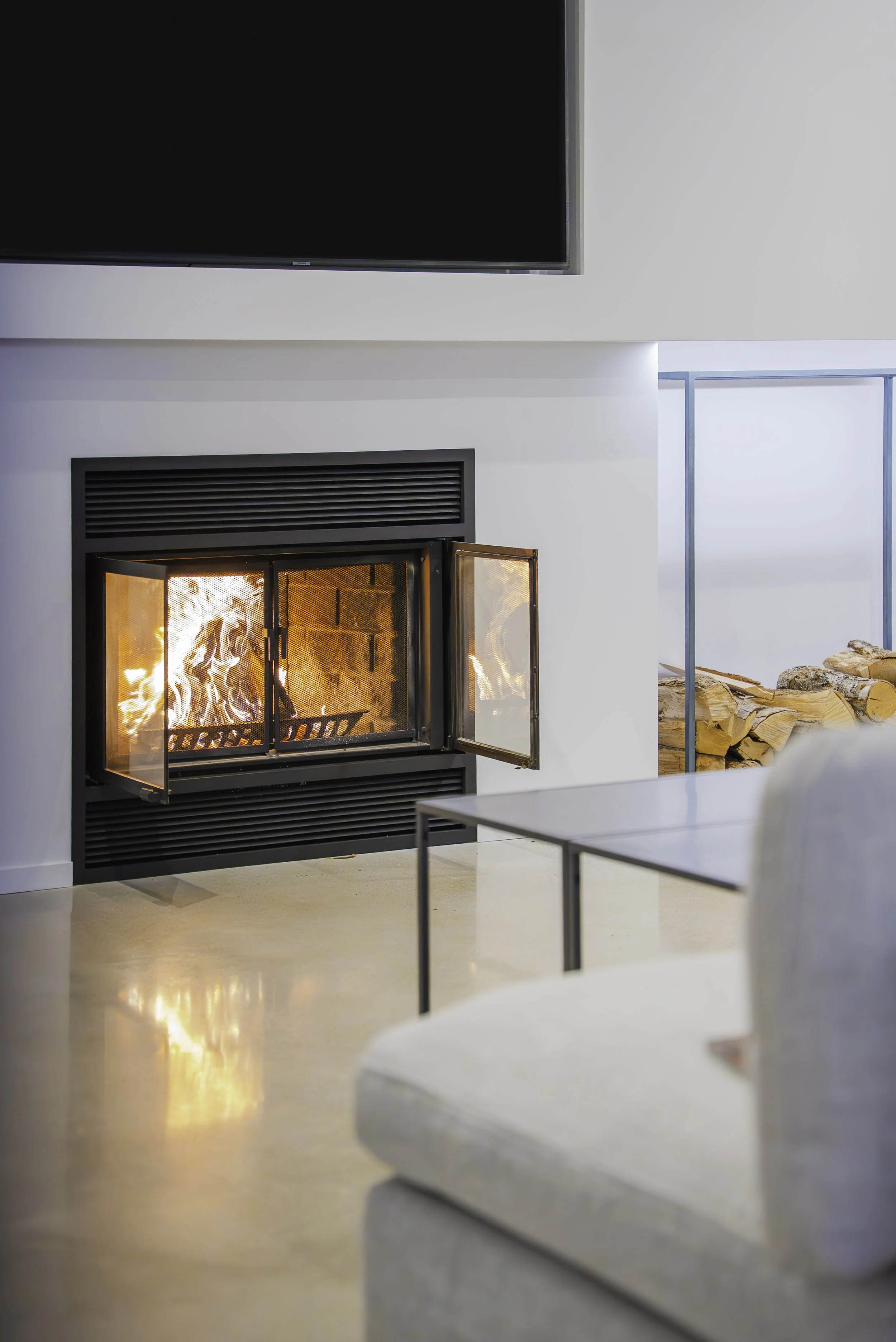 Cheminée à feu ouvert allumée dans un salon moderne avec un tapis de bois empilé à côté.