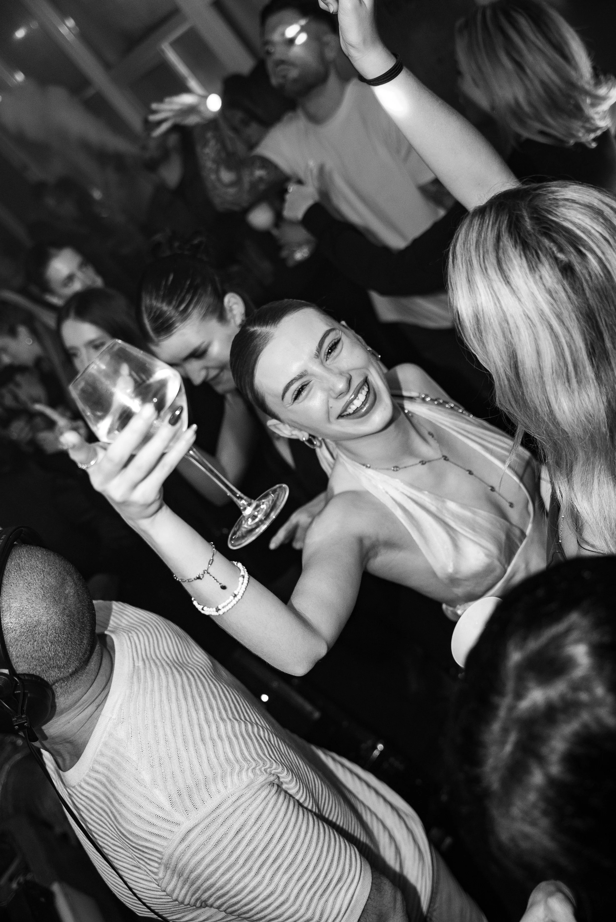 Fête en boîte de nuit avec une femme souriante tenant un verre, entourée d'autres personnes dans une ambiance de danse et de convivialité.