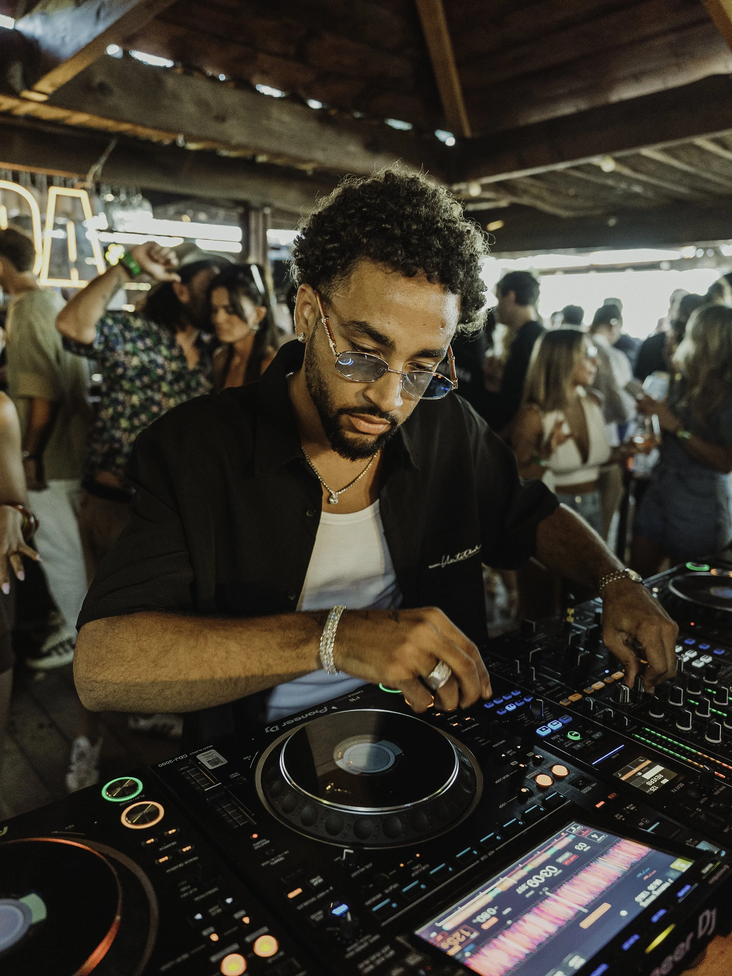 DJ en train de mixer lors d'une fête ou d'un événement, avec une foule de personnes en arrière-plan dans une ambiance animée.