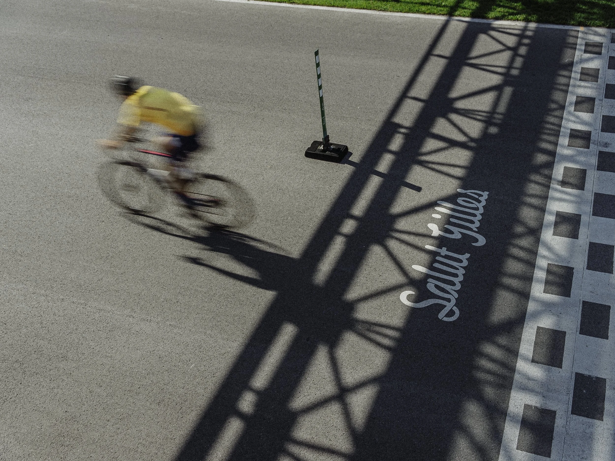 Un cycliste portant un maillot jaune roulant à vélo sous un pont shadow dans une rue, avec un panneau marqué 'sault joual' sur le sol.