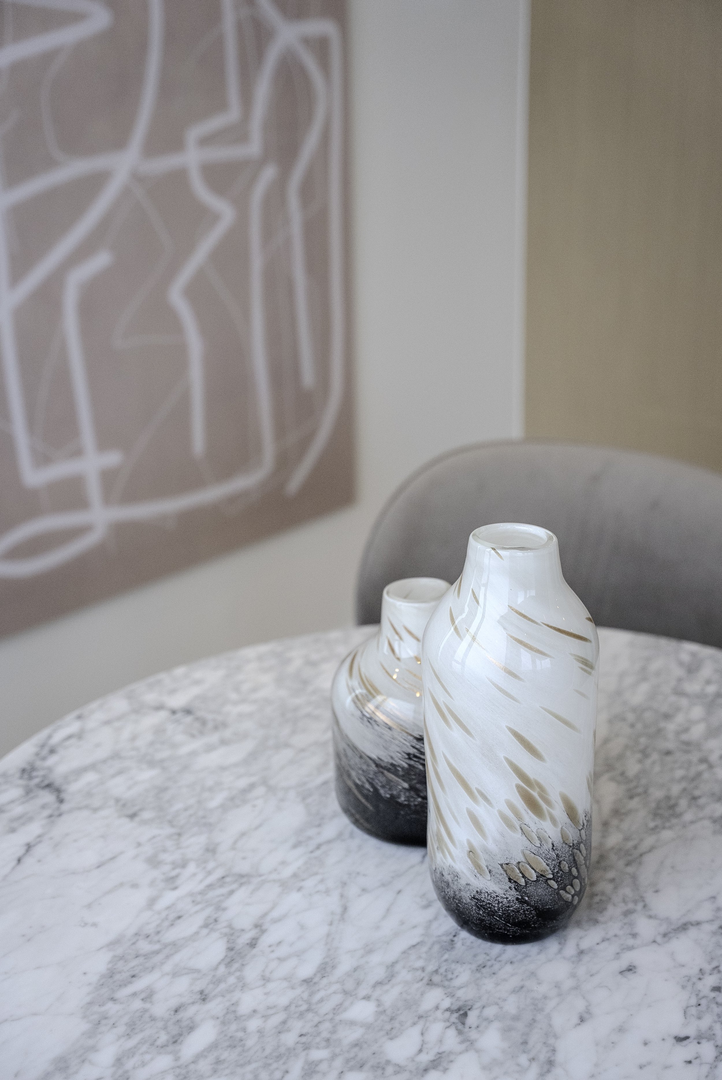 Deux vases en céramique blancs avec des motifs bruns et noirs, placés sur une table en marbre blanc, dans une pièce décorée avec une peinture abstraite au mur.
