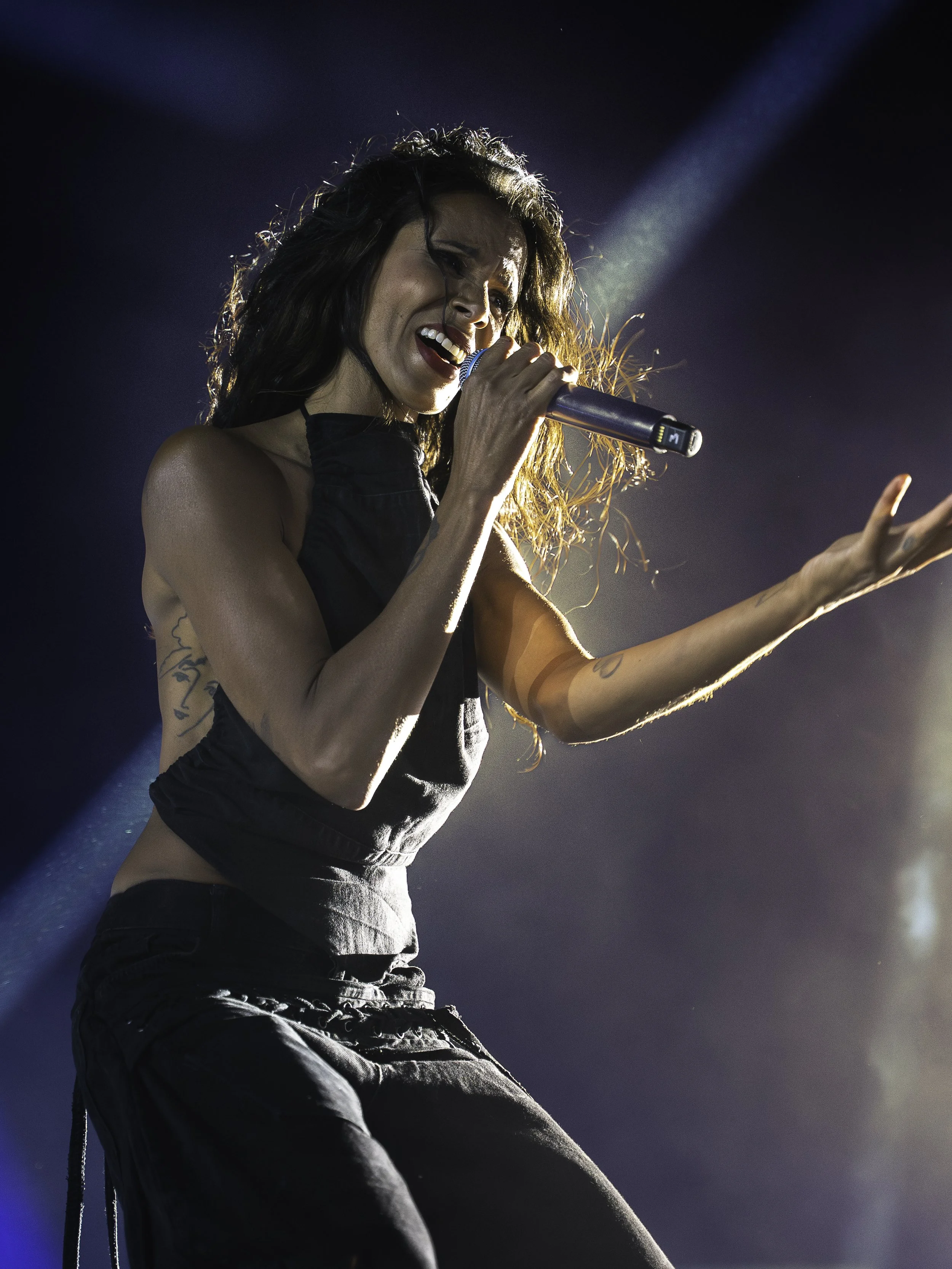 Une femme chante passionnément en tenant un microphone sur scène avec des projecteurs illuminant la scène.