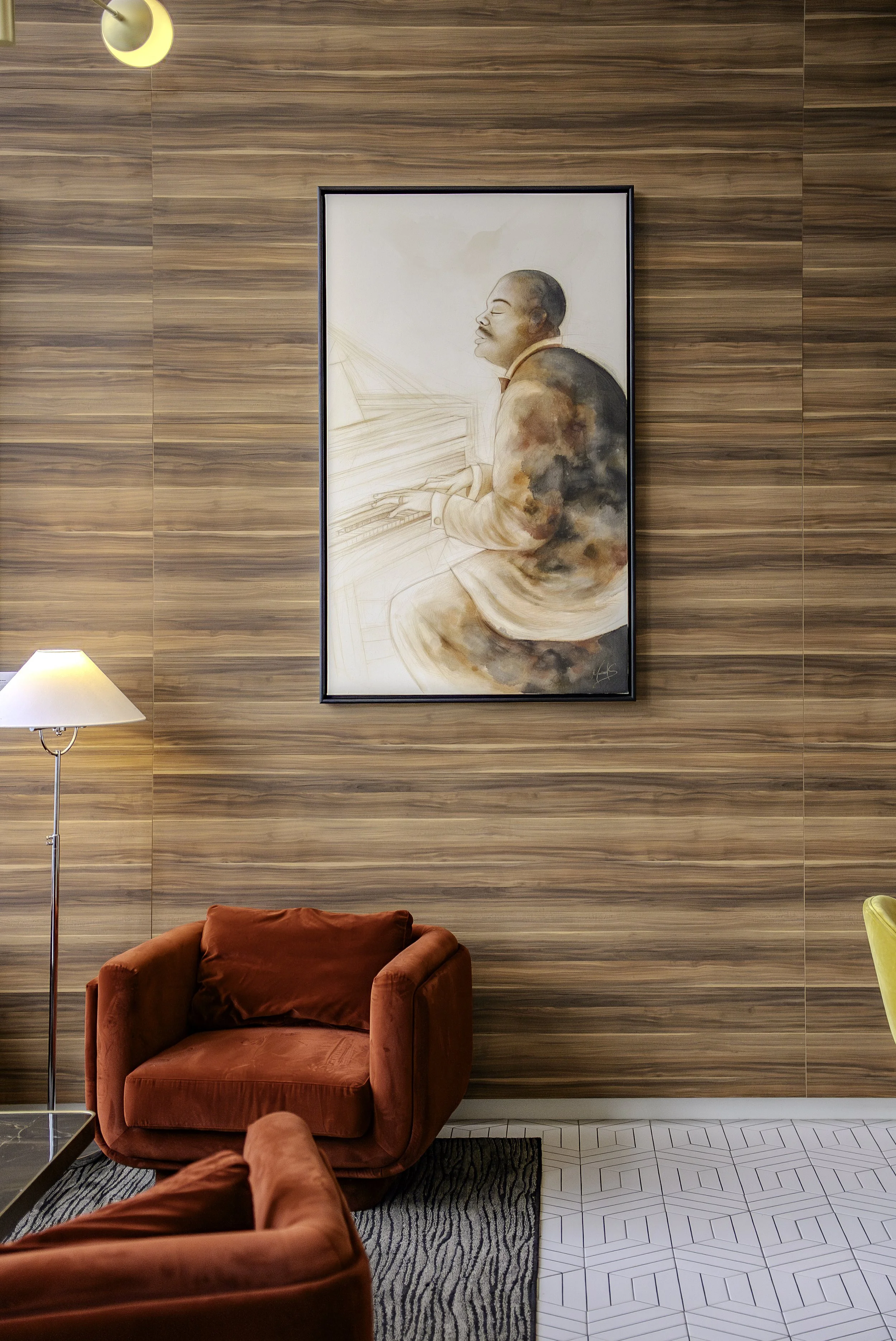 Salle de séjour avec un mur en bois, un tableau d'une personne jouant du piano, un fauteuil rouge en velours, une lampe de sol, un tapis noir et blanc, et une partie d'un fauteuil jaune.