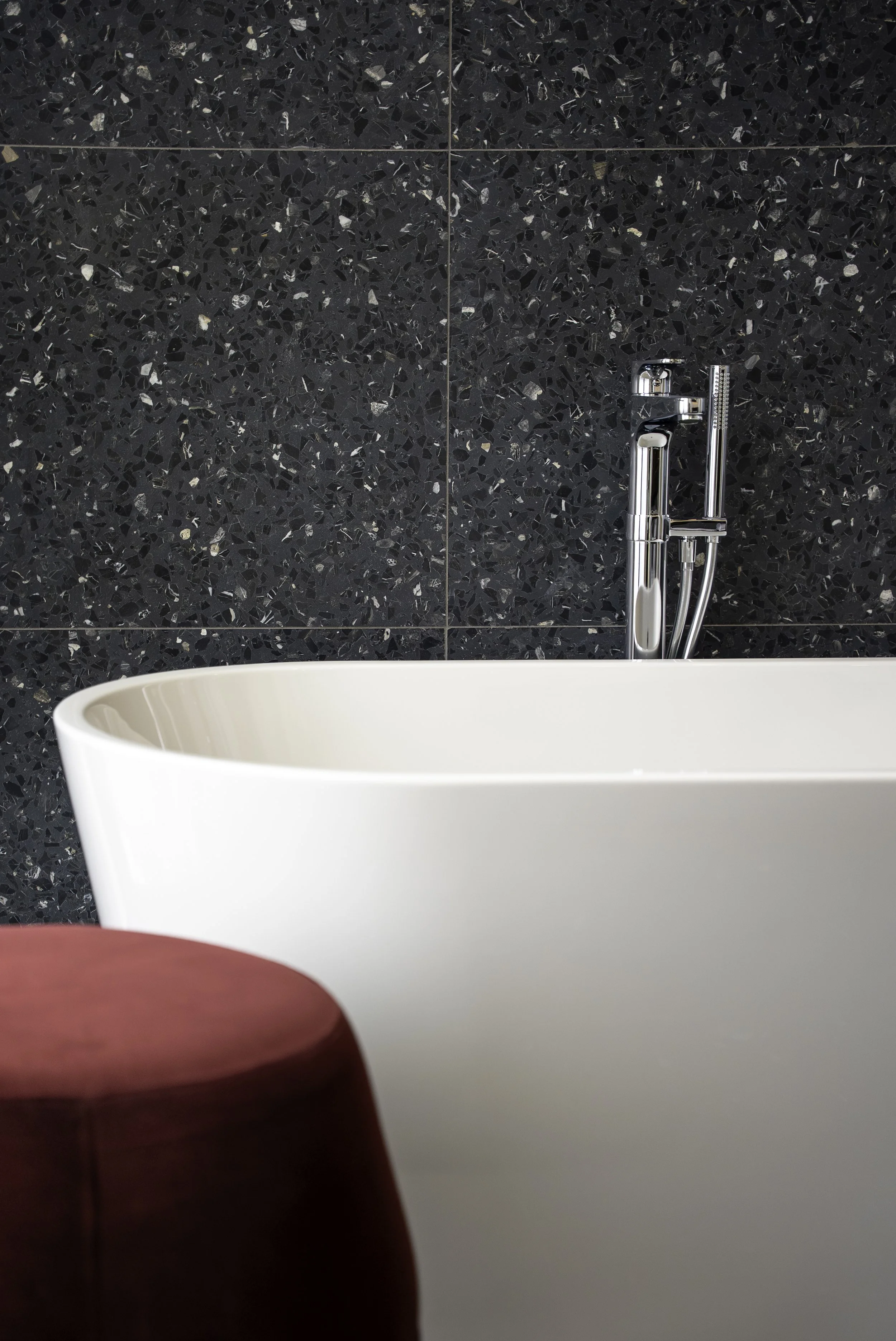 Baignoire blanche dans une salle de bain moderne avec mur en carrelage noir à motifs.