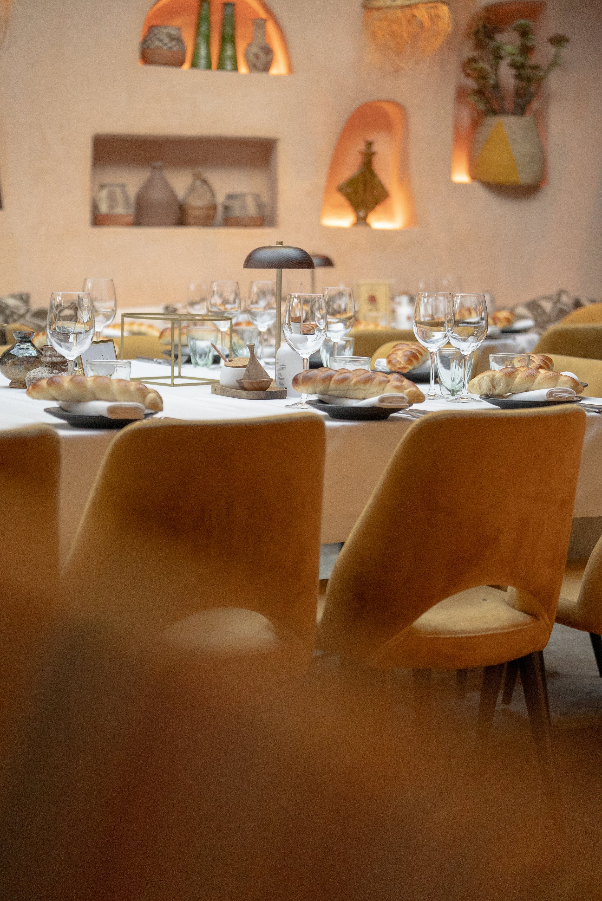 Une salle à manger élégante avec une table dressée, des verres à vin, du pain, et des décorations en arrière-plan.