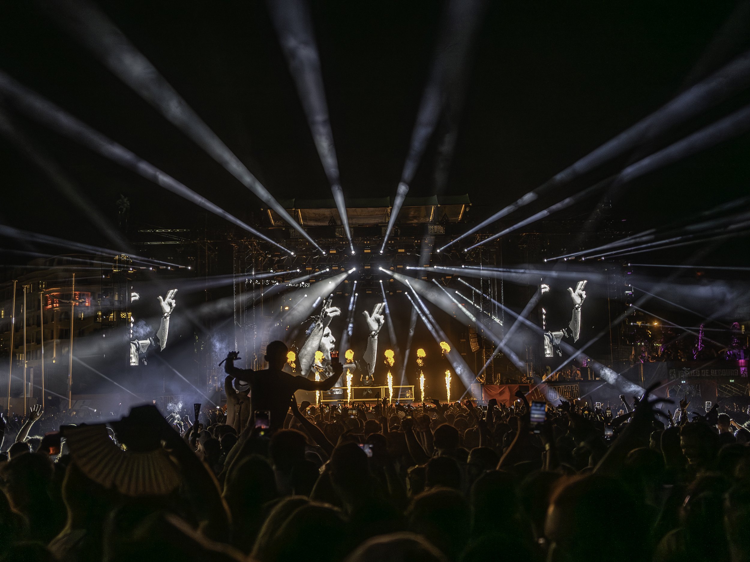 Concert à l'extérieur avec un grand public, lumières colorées et écrans géants. 