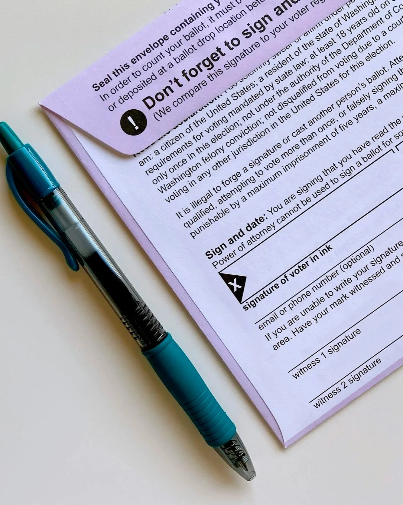 A pink voter registration form with a blue pen resting on top of it. The form contains sections for signature and witness signature and contains a warning not to forge the signature. The form emphasizes the illegality of forging a signature and lists instructions for filling it out.