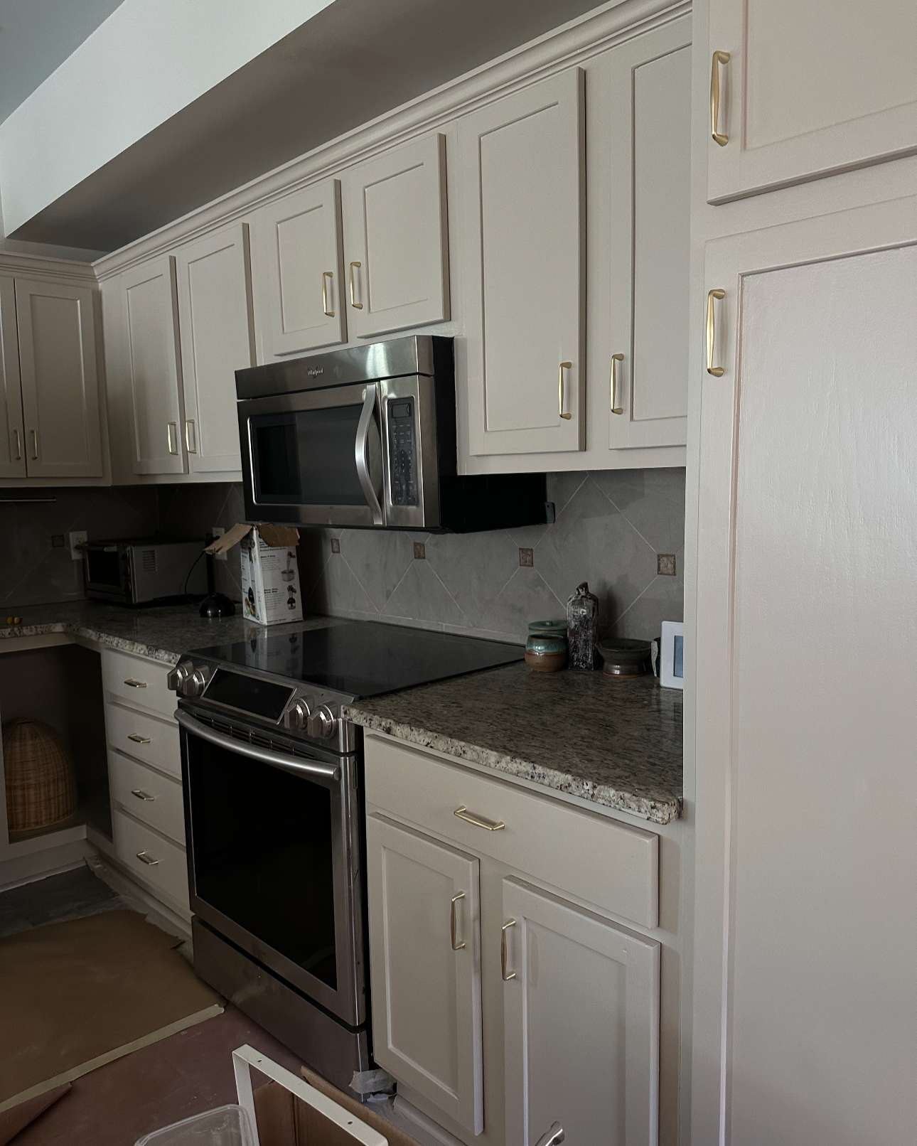 A kitchen corner with white cabinets, a stainless steel microwave, a stove, and various small appliances and items on the countertop.