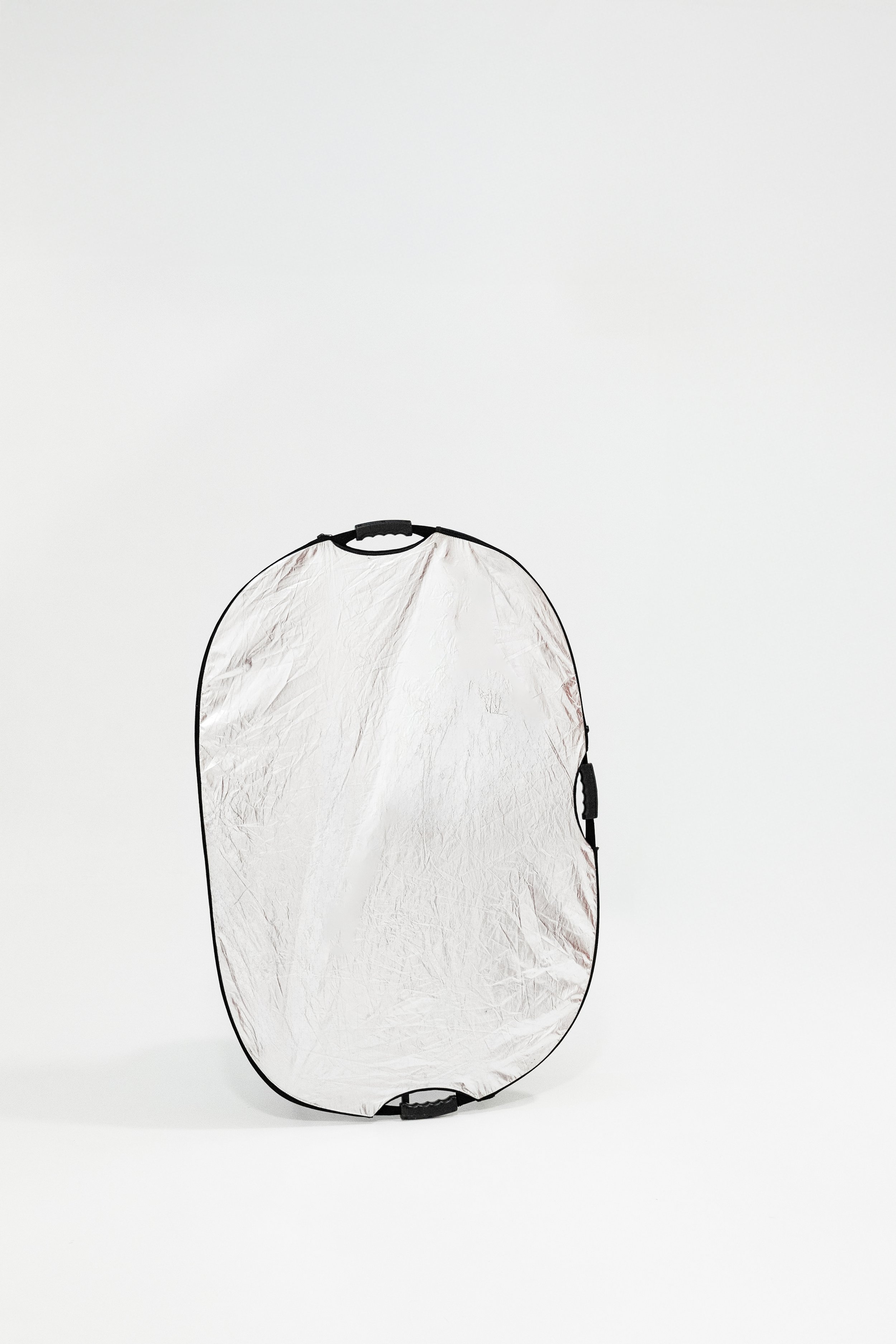 A collapsible silver reflector with black trim standing upright on a white background.