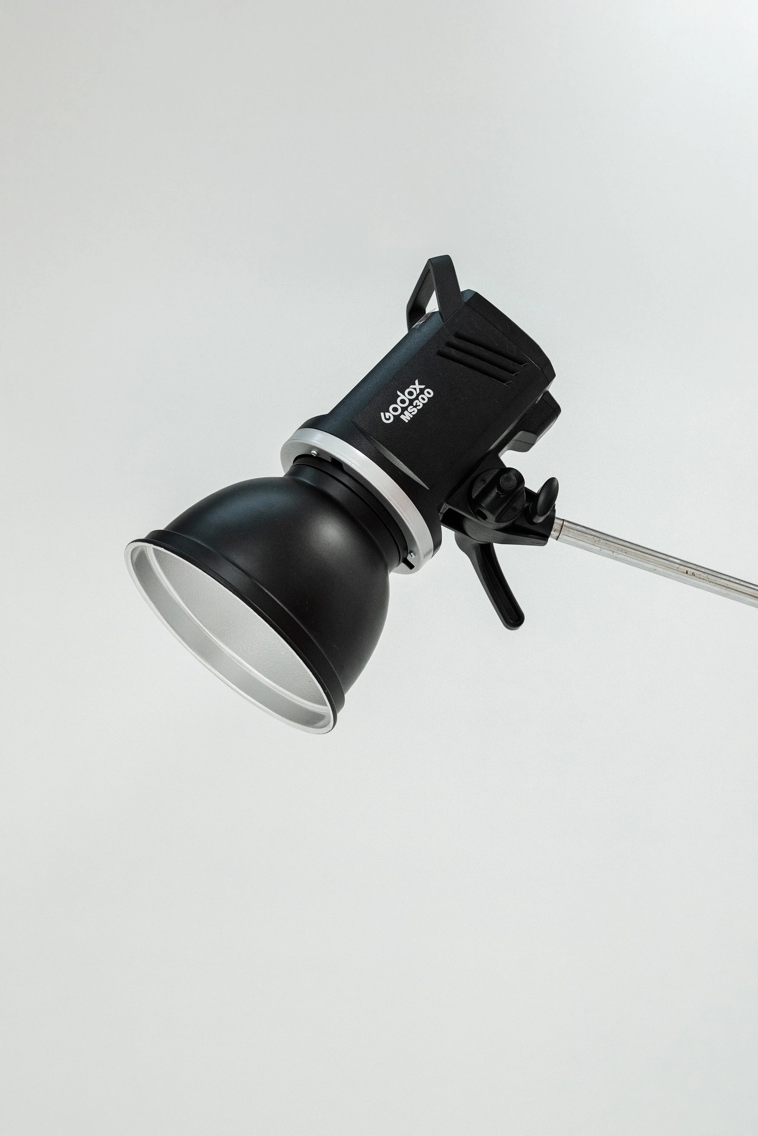 Studio flash light mounted on a metal stand against a plain light grey background.