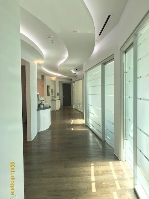 Modern hallway with curved white ceiling and wooden flooring, lined with large glass sliding doors covered with frosted blinds.