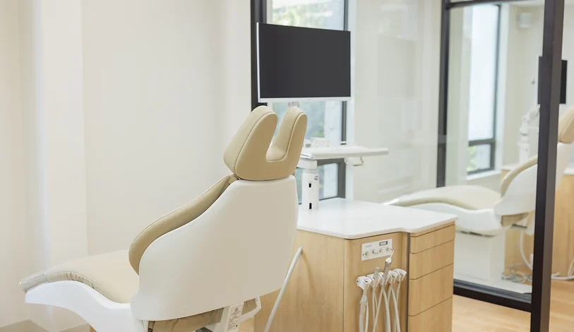 Dental examination chair in a modern dental clinic with a large monitor and a wooden cabinet with dental tools.