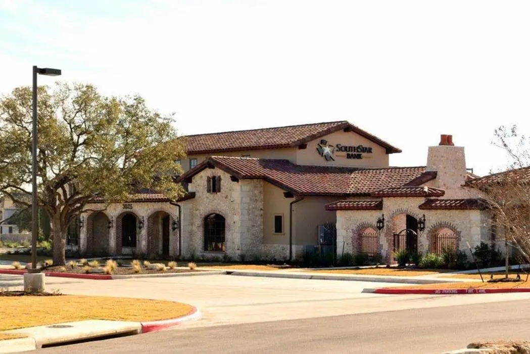A single-story building with a sign that reads "SouthStar Bank," featuring a tan stucco exterior, red tile roof, and arched windows and doors, situated in a suburban area with a large tree and parking lot in front.