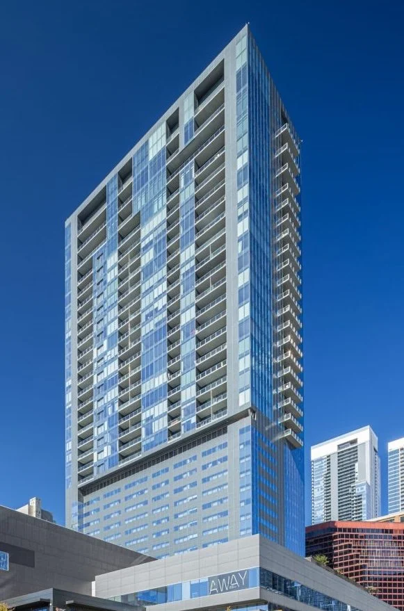 A tall modern high-rise building with a glass exterior against a clear blue sky.