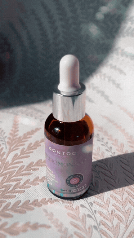 A small amber glass dropper bottle with a white dropper cap, placed on a patterned fabric with sunlight casting shadow.