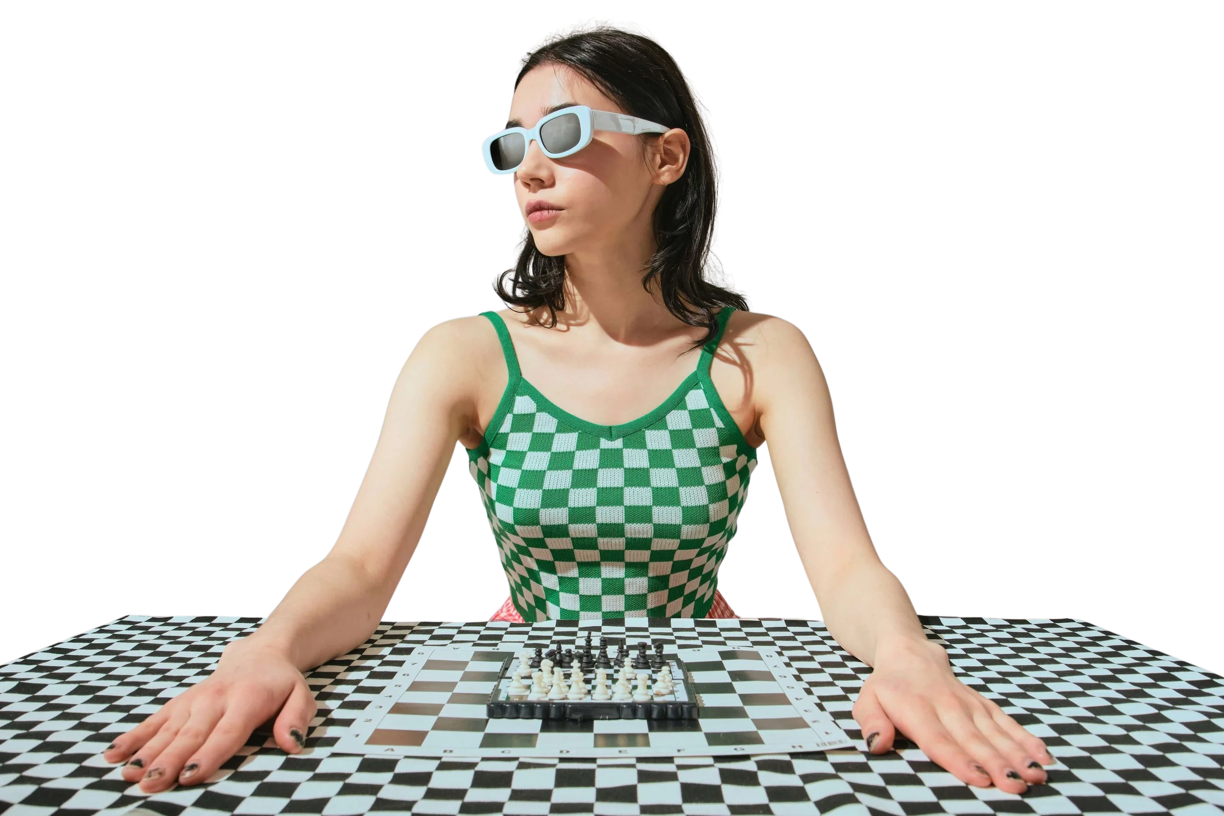 Woman with dark hair wearing sunglasses and a green checkered top seated at a checkered chessboard.