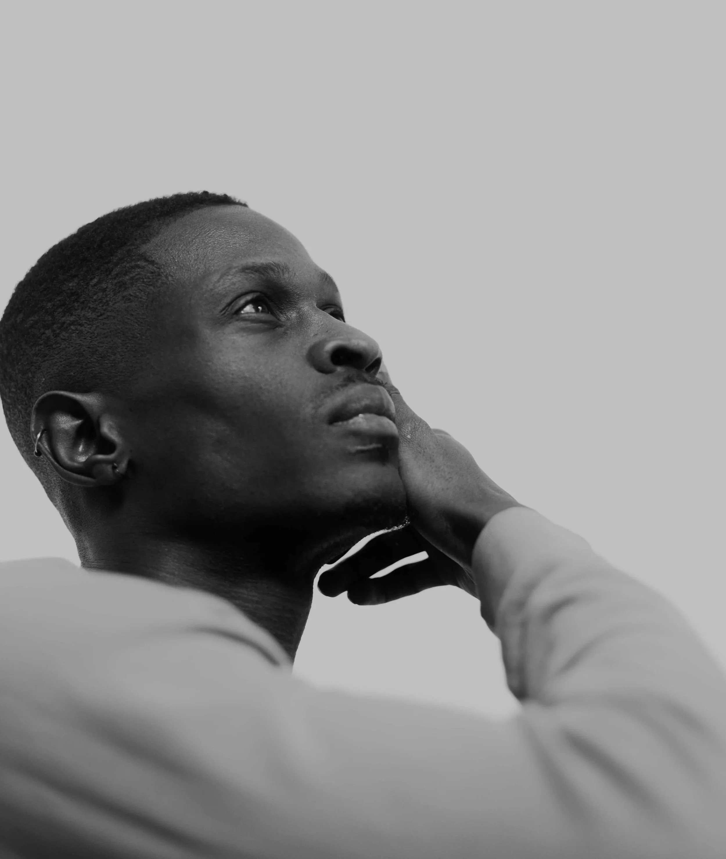 Close-up of a person with short hair looking upward, with hand resting on face, in black and white