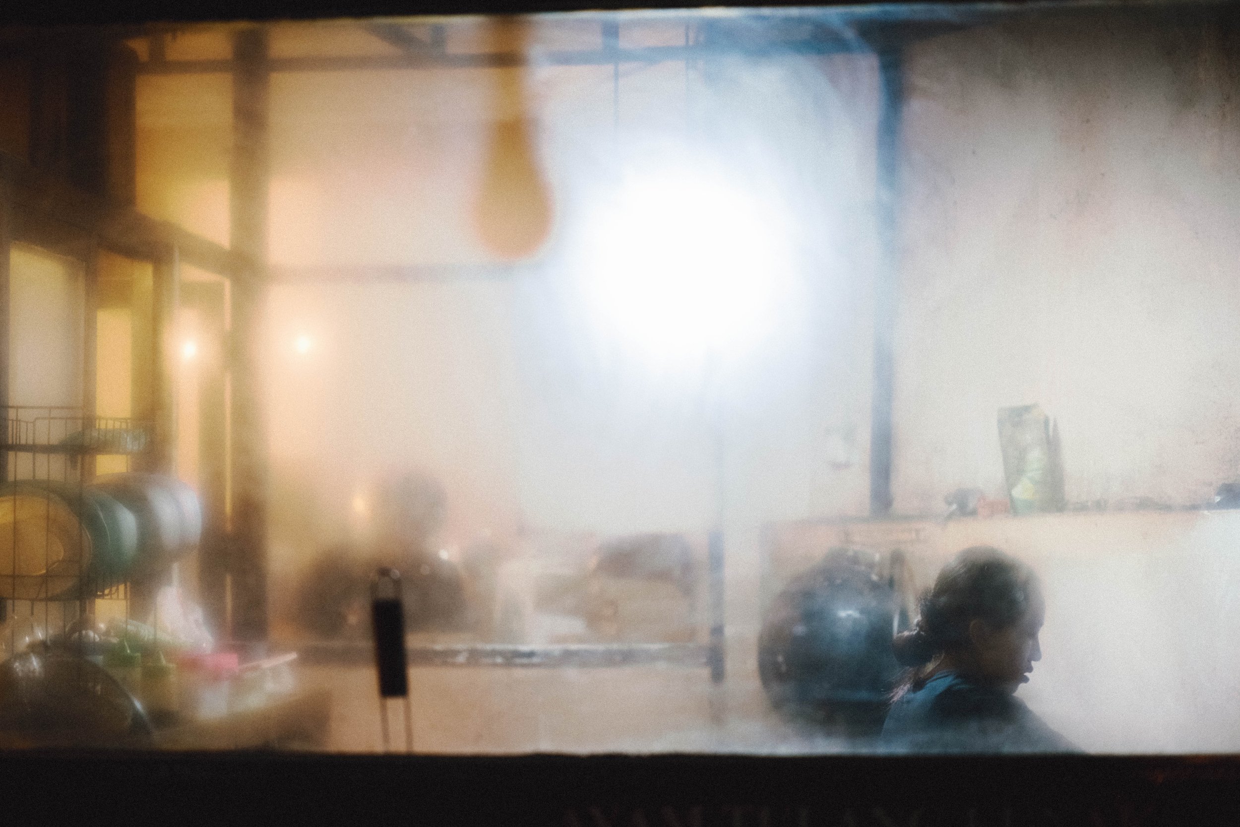 A blurry image taken through a window showing a room with furniture and some debris, possibly during a storm or fire, with smoke or fog obscuring the details.