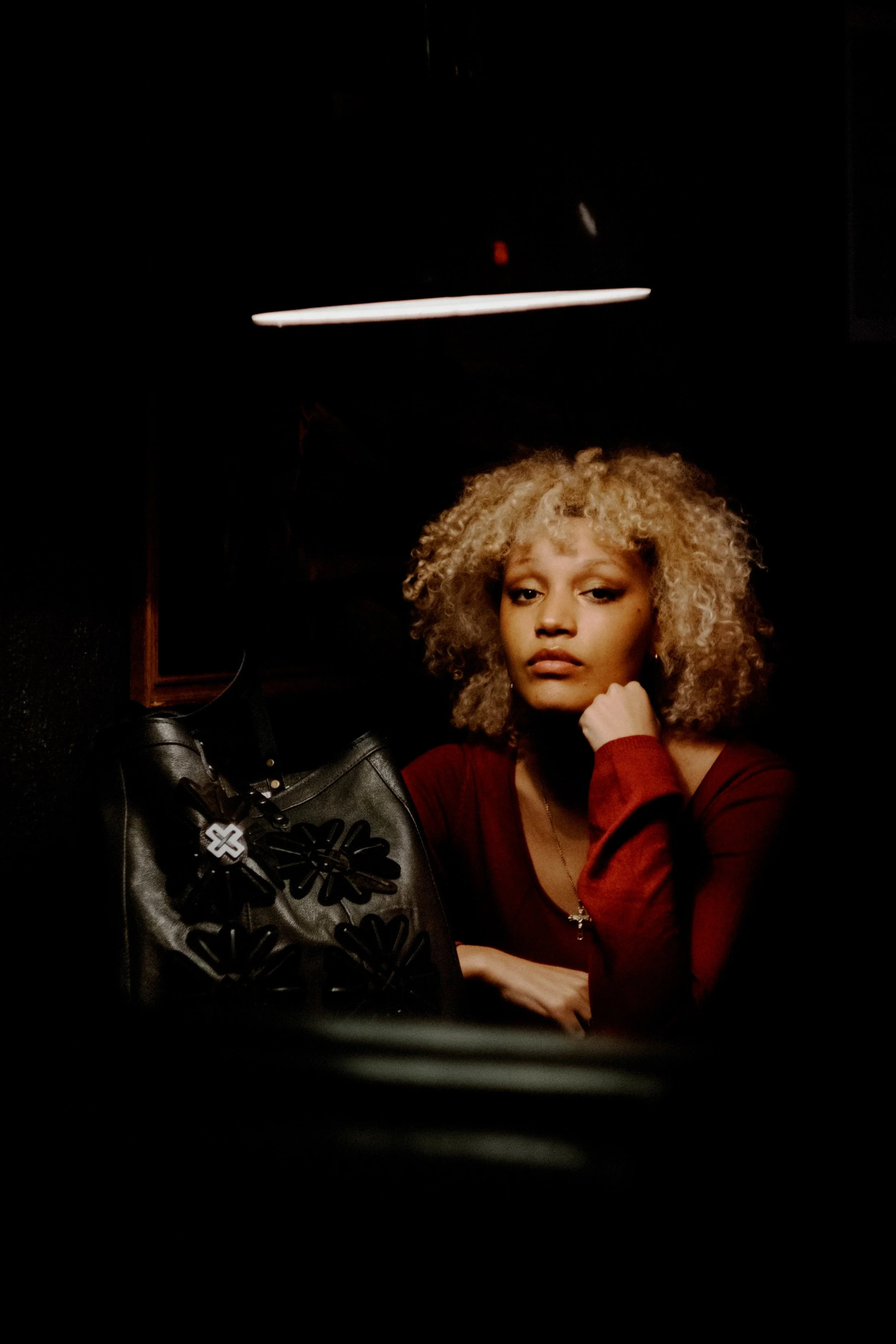 A woman with curly blonde hair sitting at a table in a dimly lit room.