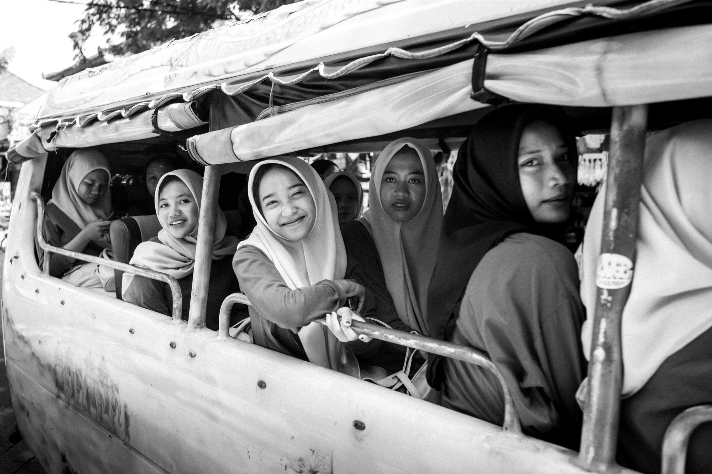 Several women and girls are riding on an outdoor open-sided vehicle, some wearing headscarves.