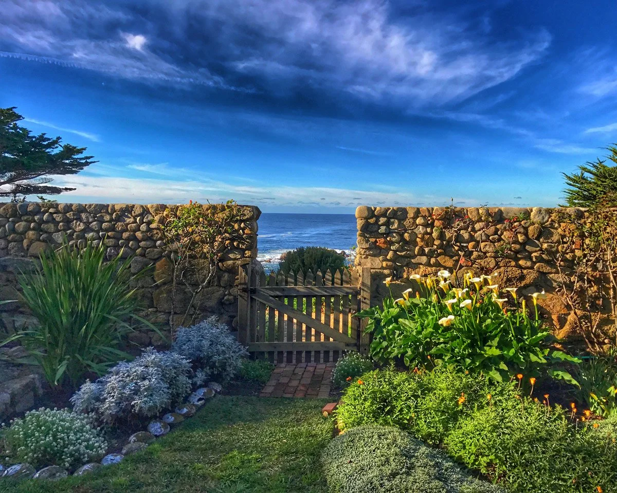 Tor House garden with stone walls and a wooden gate with ocean and sky in the background