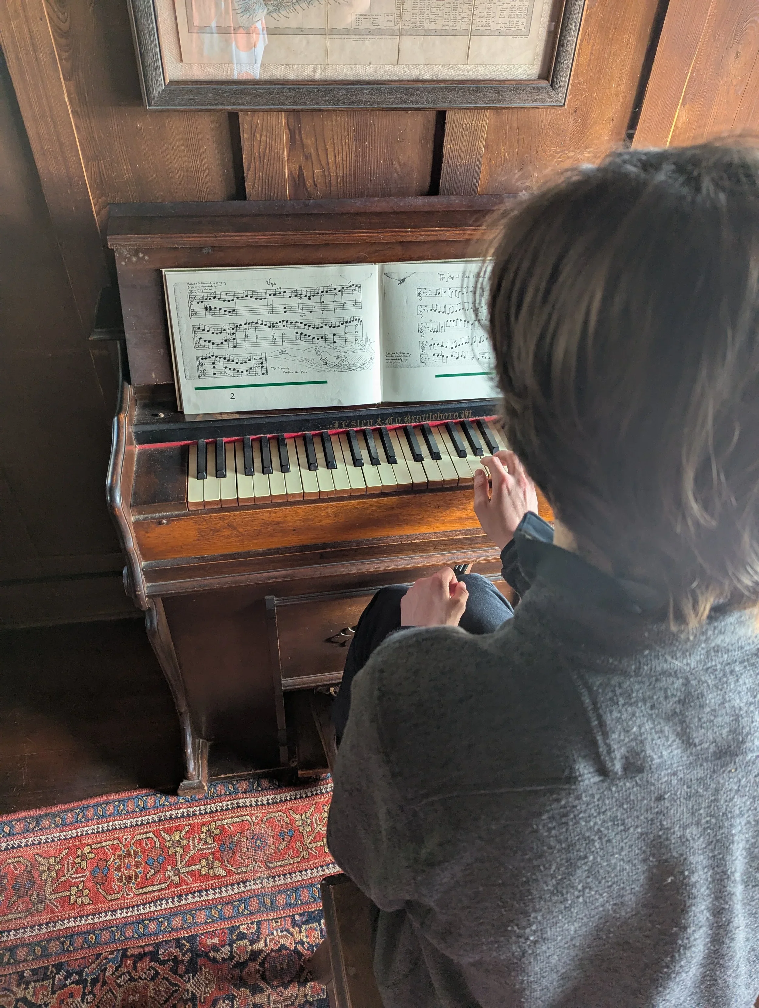 Person playing a vintage wooden piano with sheet music open on the music stand.