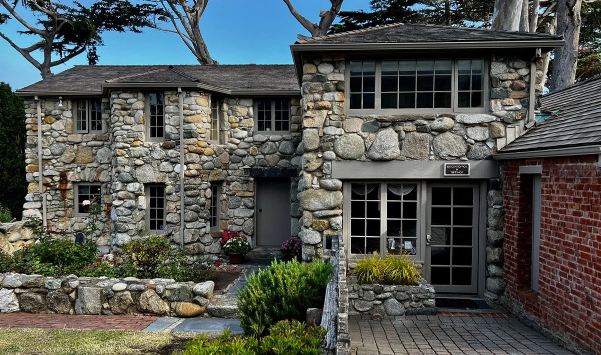 Stone and brick building with multiple windows, a door, and a garden in front.