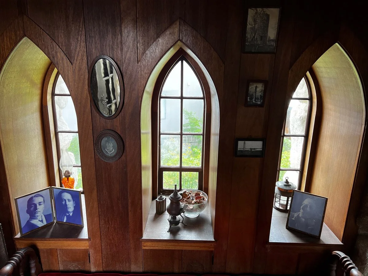 Wood-paneled wall with three arched windows, framed photographs, and decorative items on the ledge.