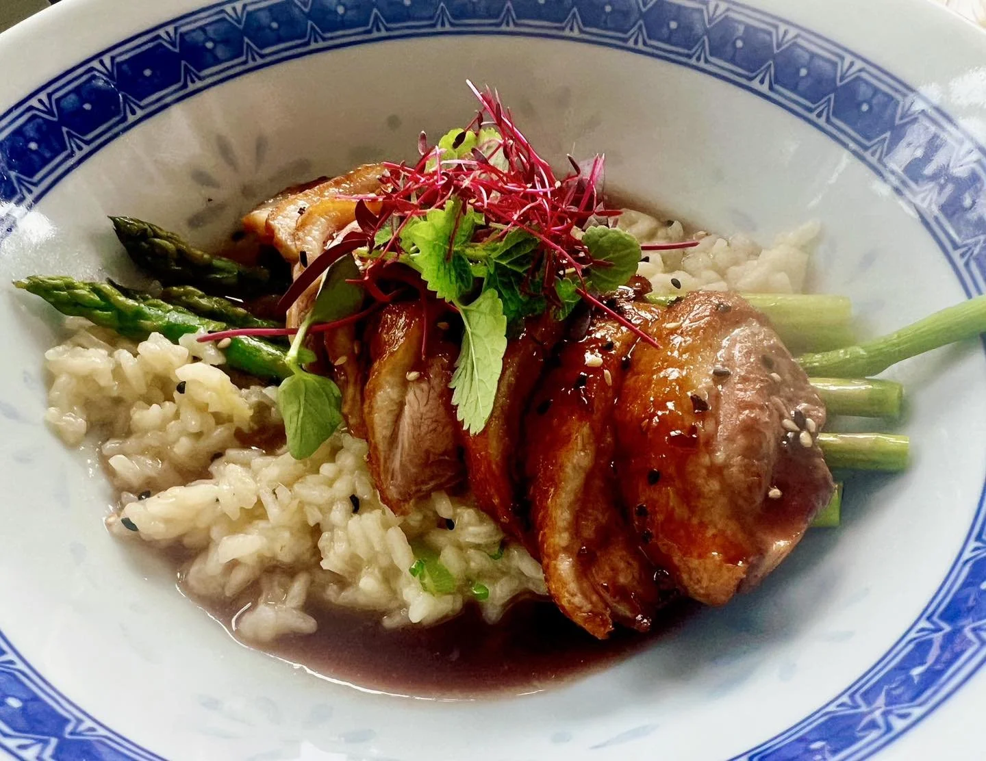 A bowl of gourmet rice pudding topped with grilled vegetables, sliced roasted meat, and microgreens.