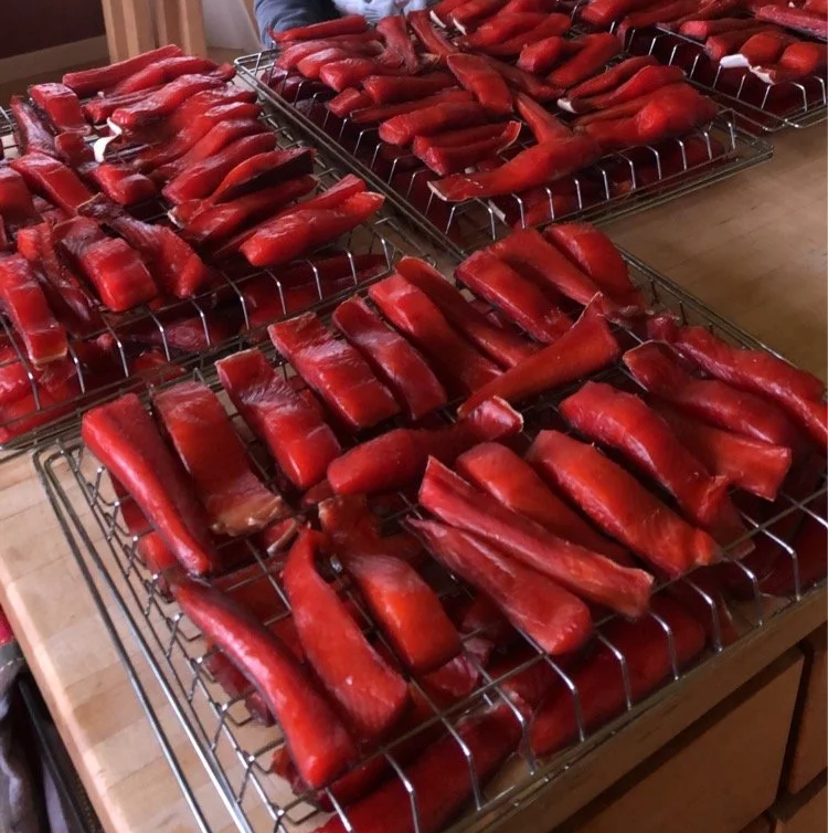 Several racks of smoked or dried red peppers laid out on wire cooling racks on a wooden countertop.