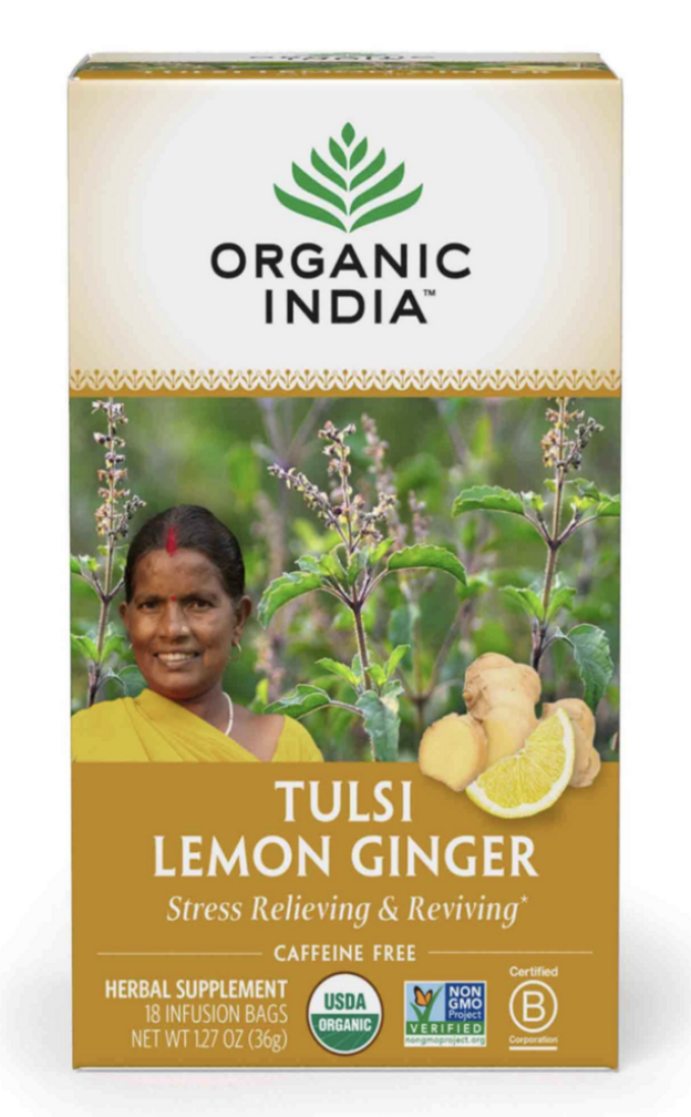 Box of Tulsi Lemon Ginger herbal supplement with a smiling woman in a yellow sari, ginger root, and lemon wedge, set against a background of basil plants.