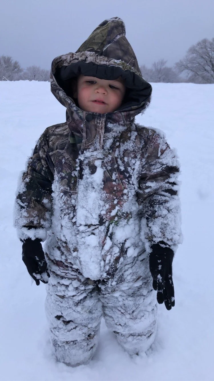 Toddler in snowsuit covered in snow.